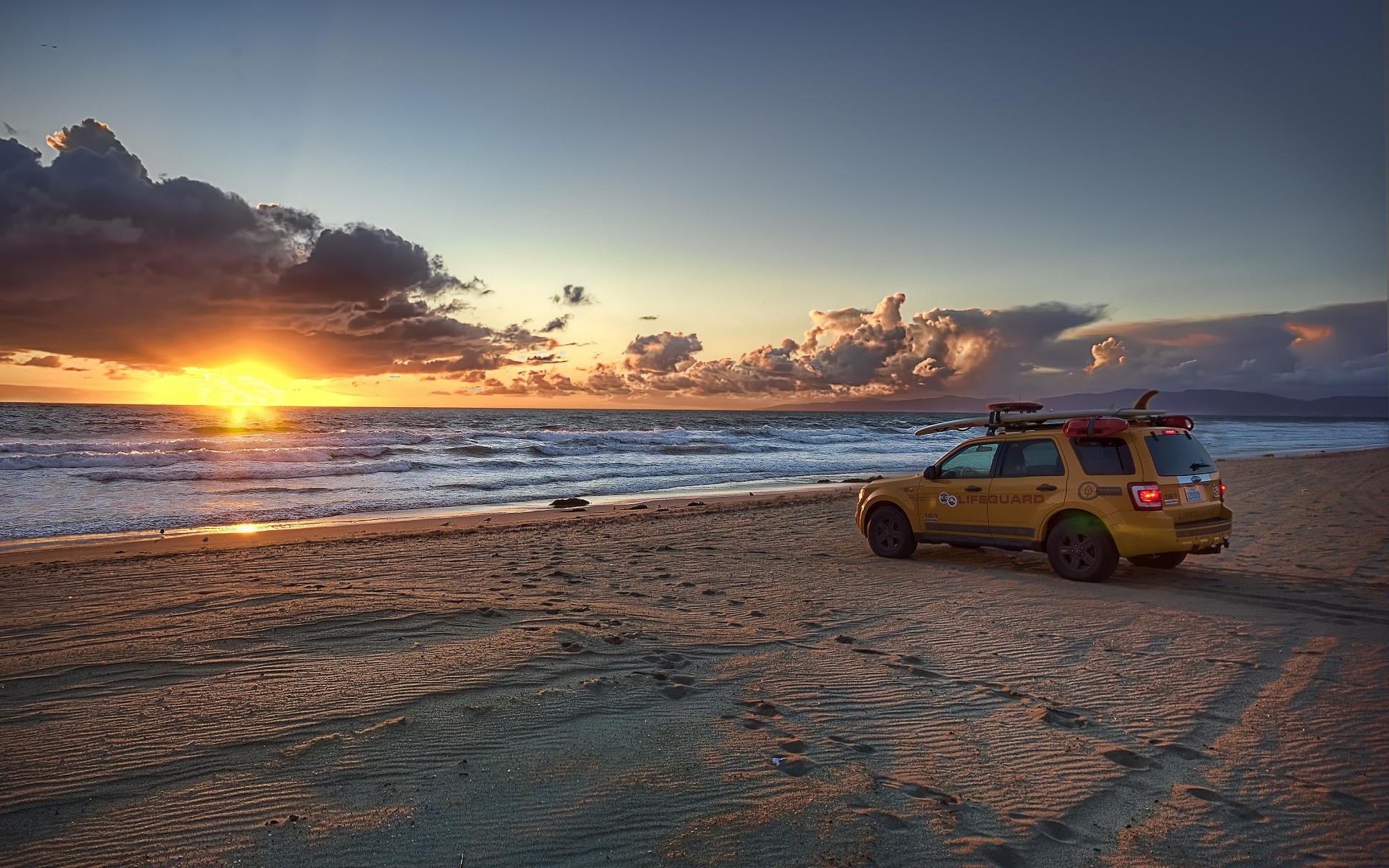 Sunset on the beach, yellow SUV on the sand.