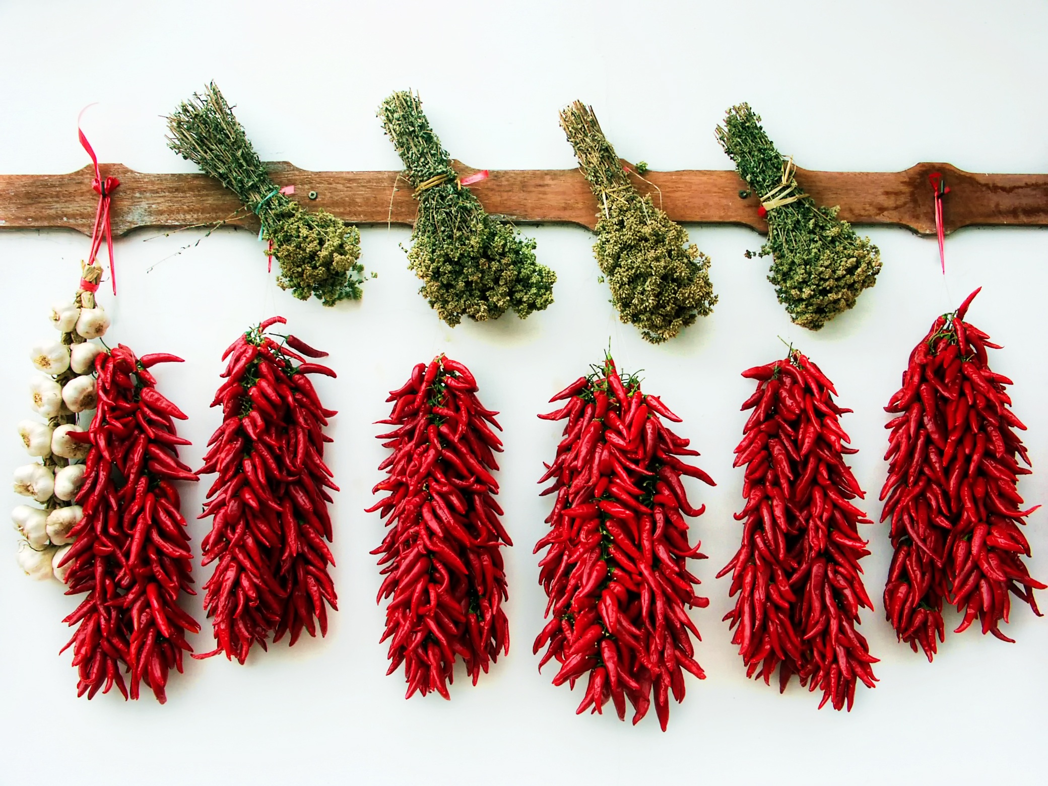 Free photo Red peppers with garlic and spices hang on the white wall