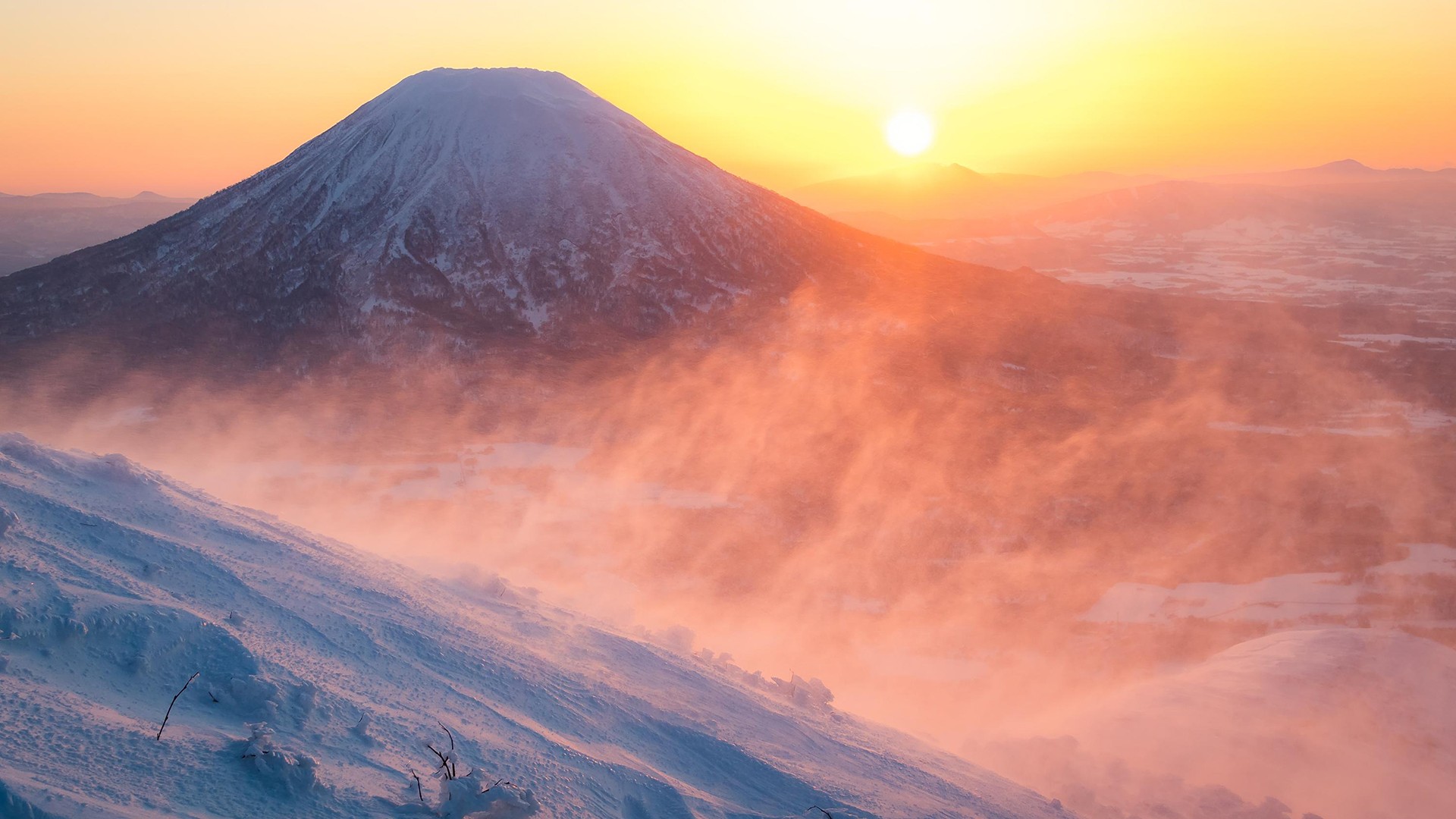 The snow-covered Klyuchevskaya Sopka at sunset, the slopes are shrouded in haze, the sky is tinged with warm shades.