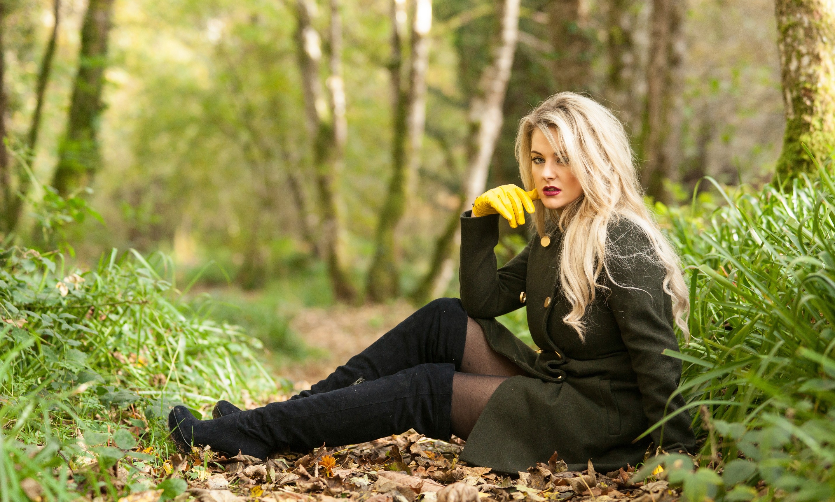 一个穿着绿色外套的金发女孩坐在落叶上
