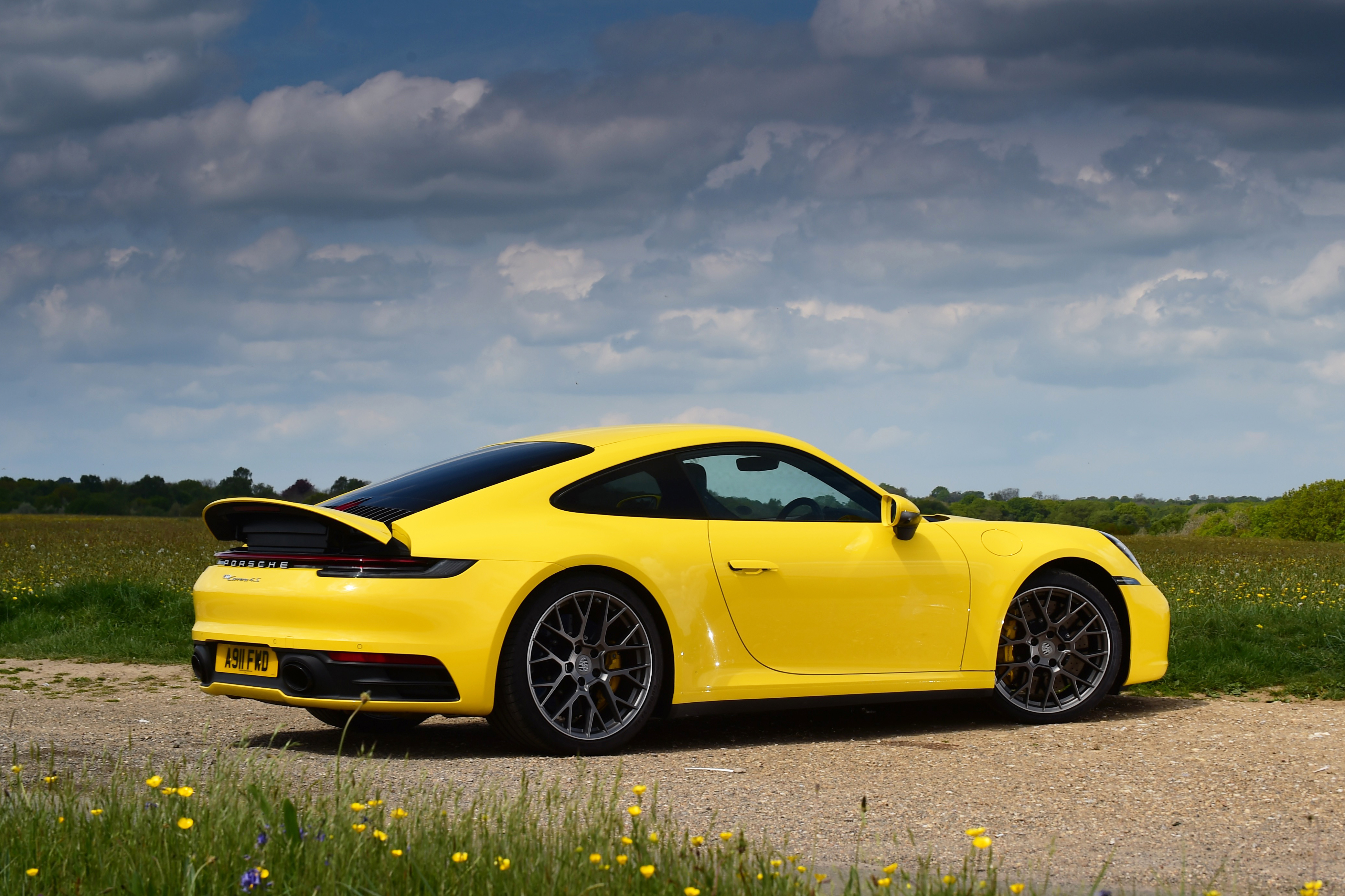 A yellow Porsche 911 with gray rims stands on a dirt road