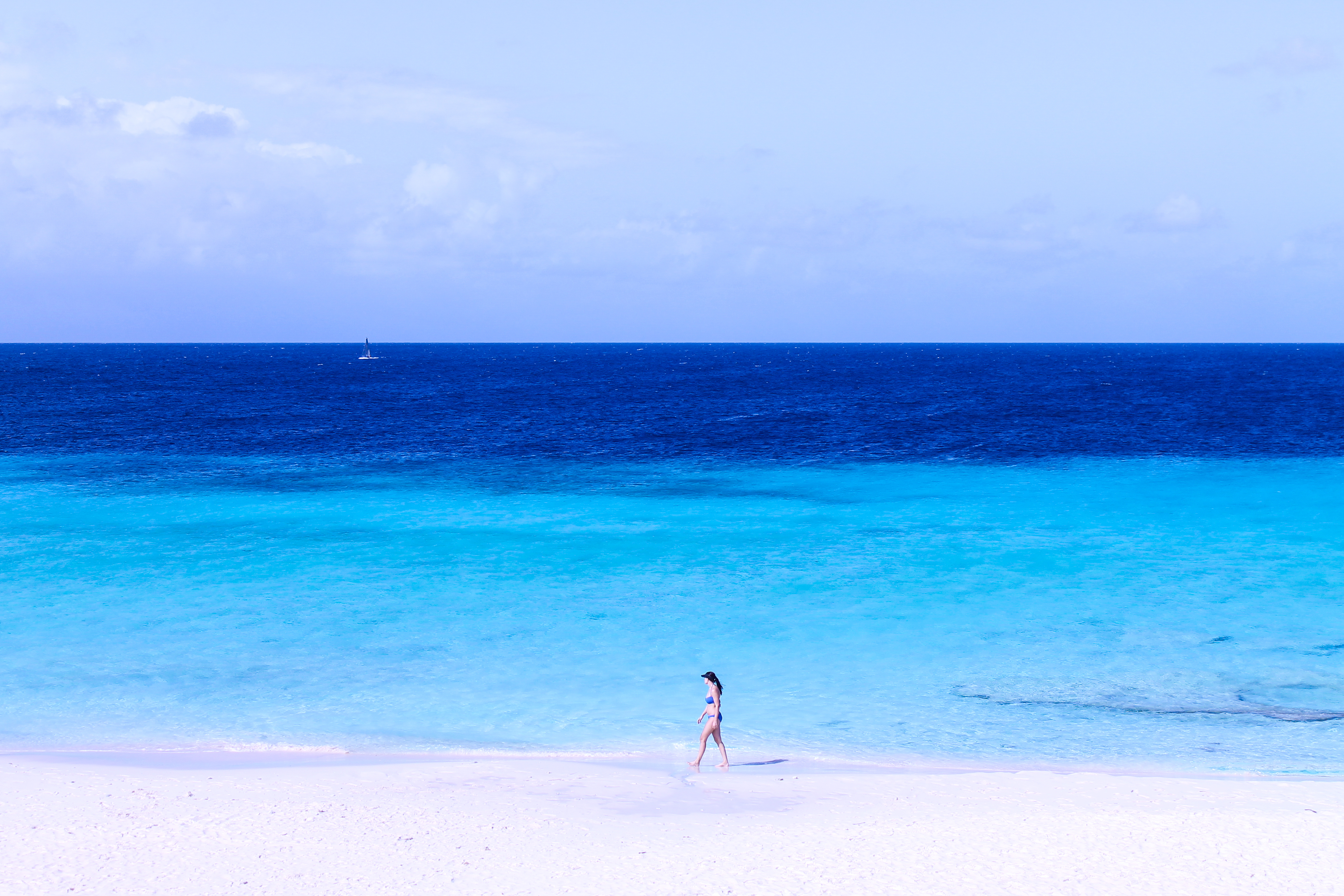 A girl walks along a sandy beach at the seaside wearing a cap