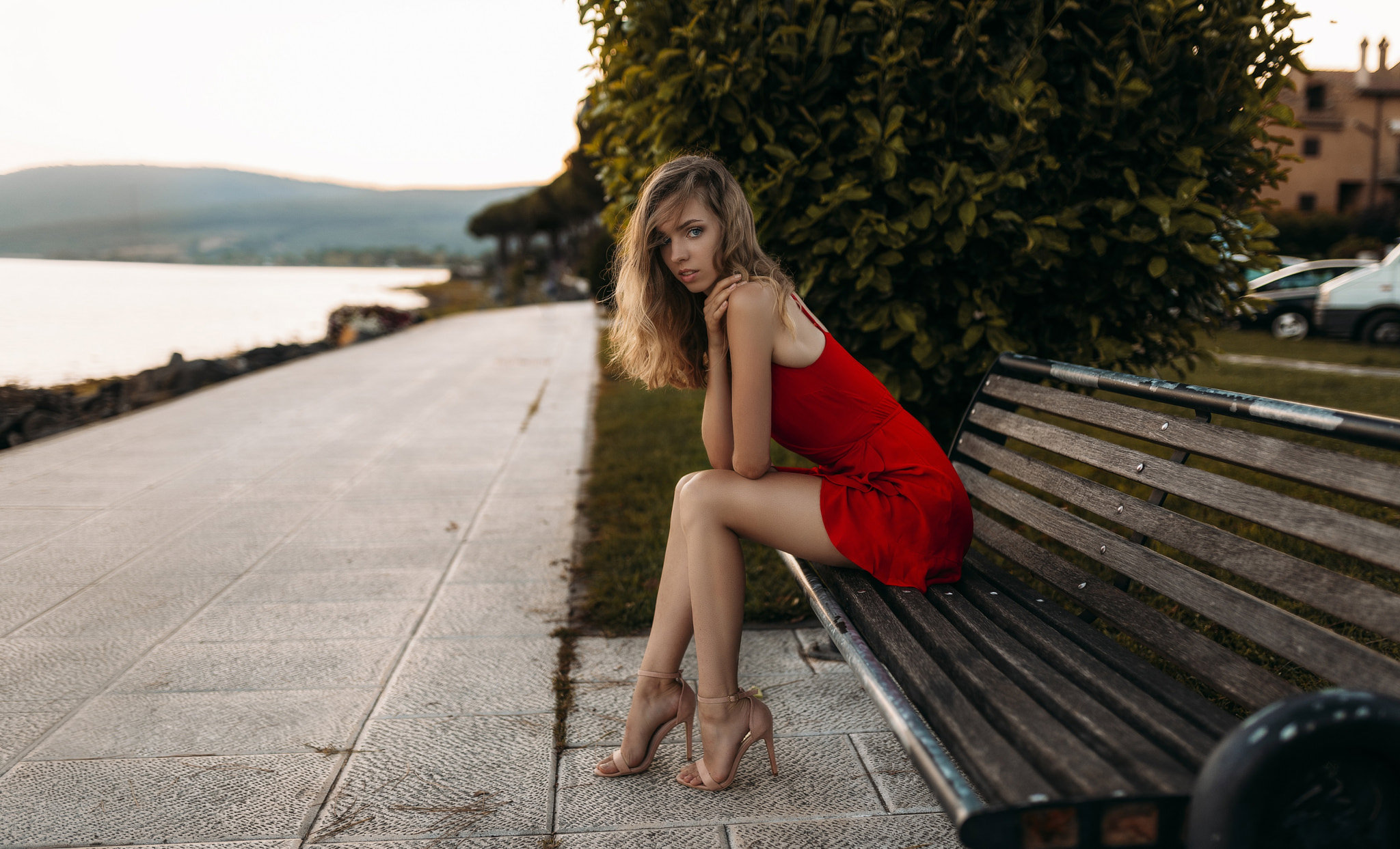 A beautiful model in a red dress sits on a bench