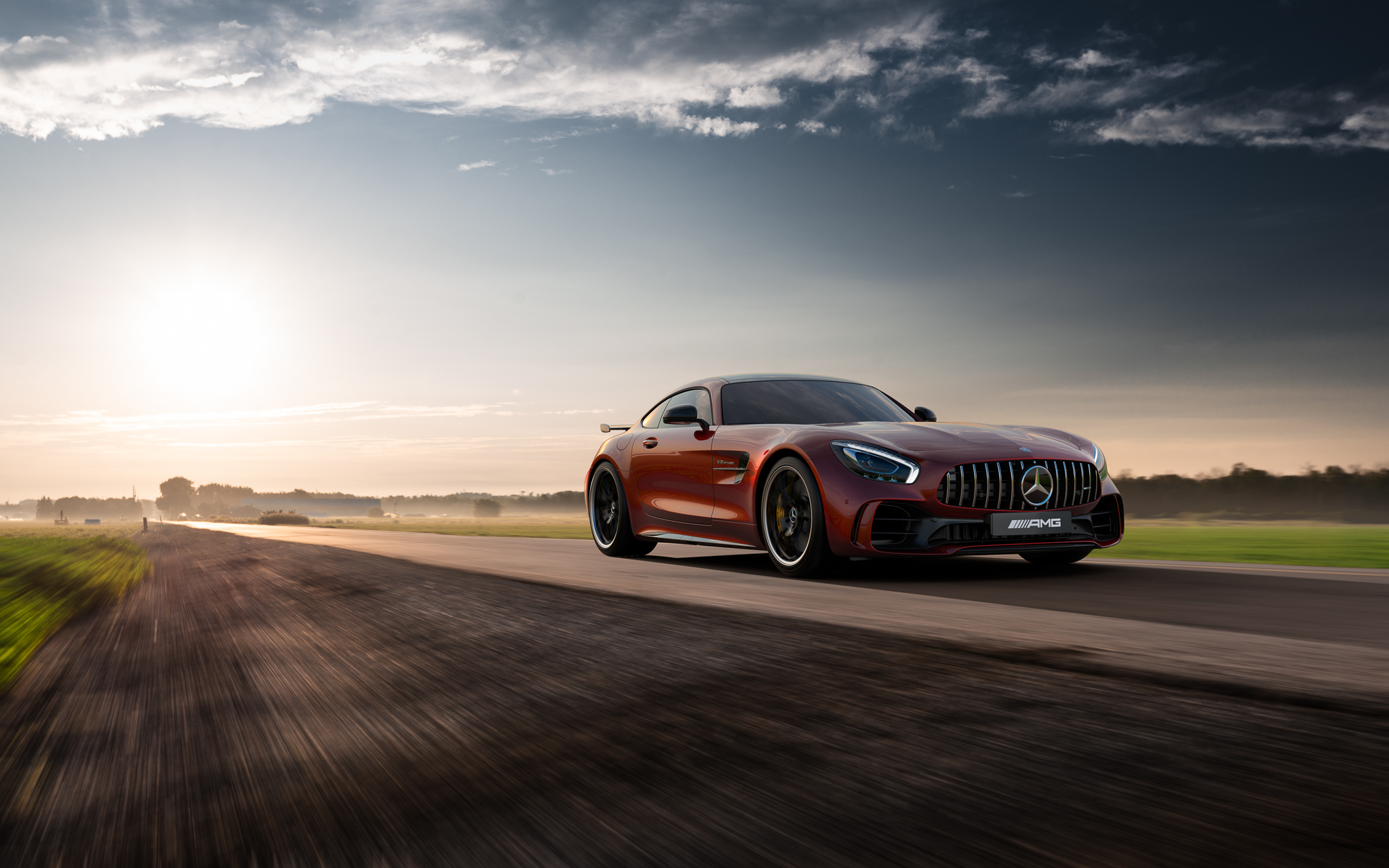 Free photo Red Mercedes AMG GTR driving down the road at sunset