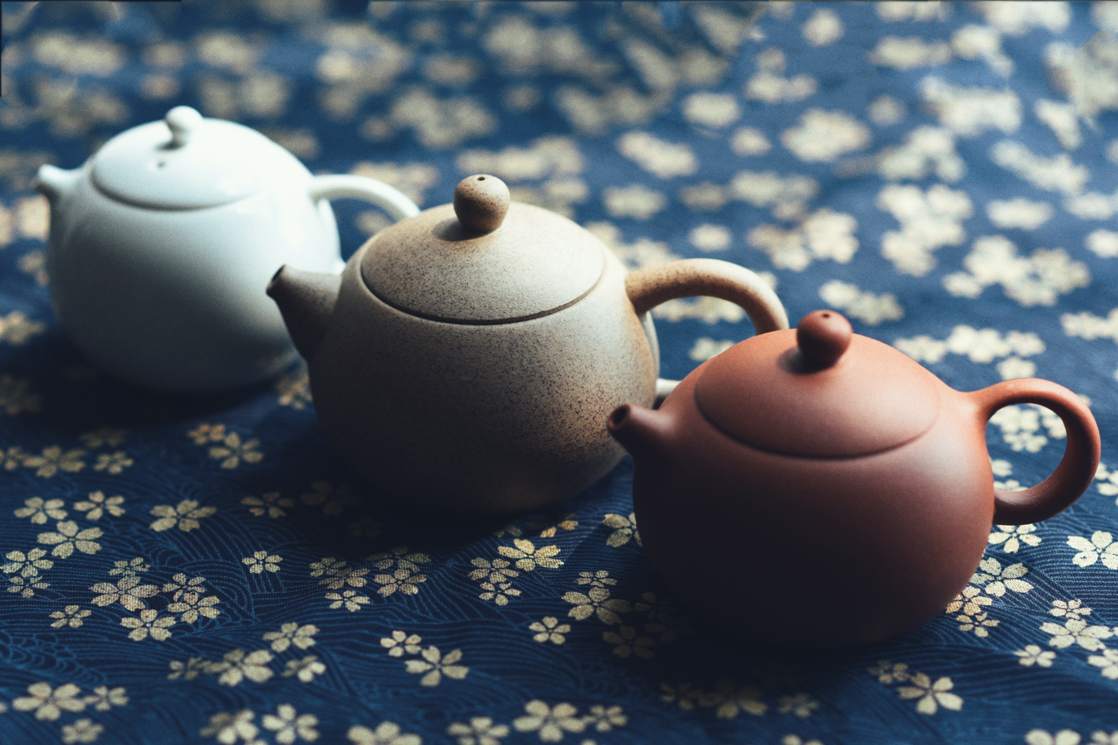 三只陶瓷茶壶立在蓝色花卉织物上