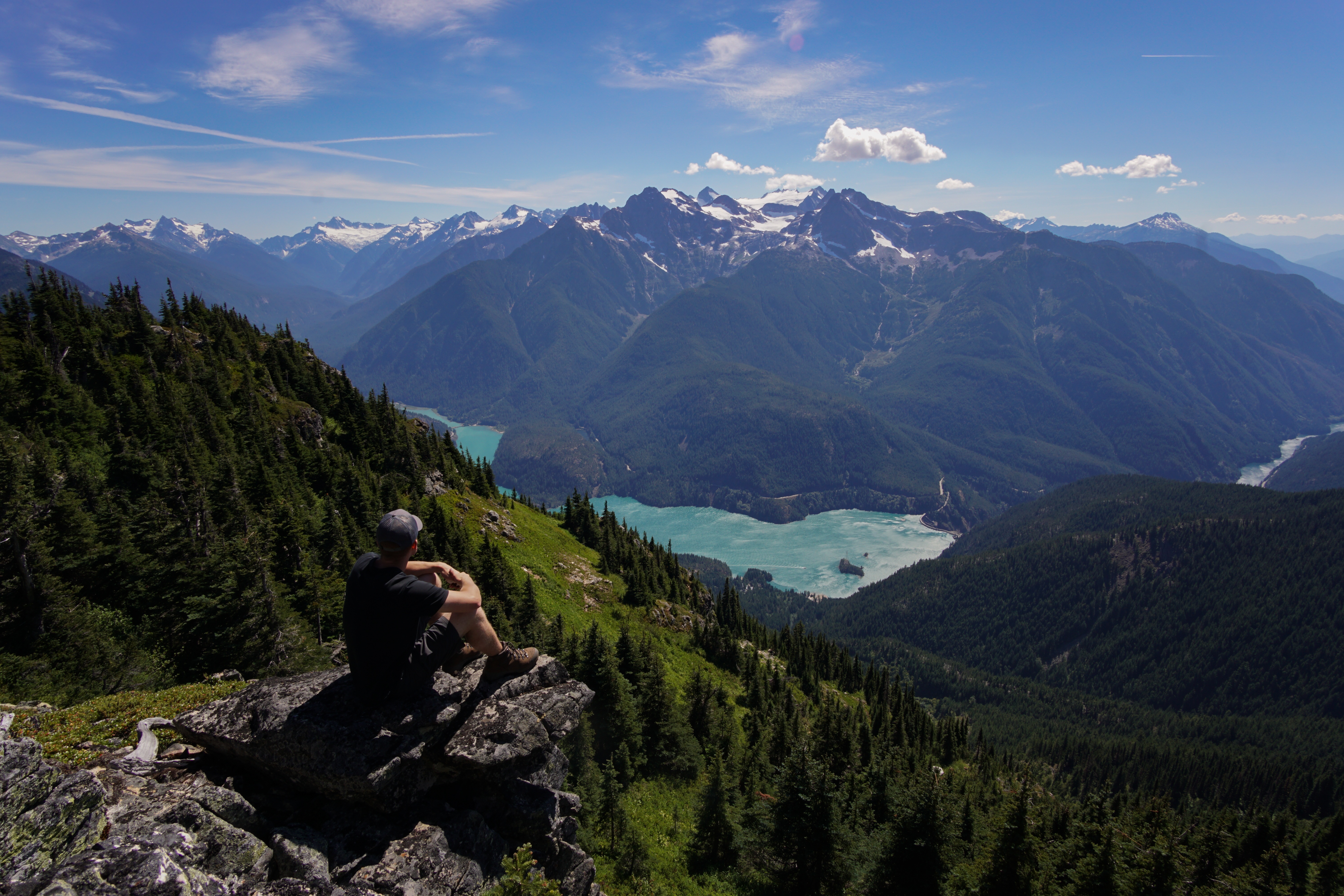 Free photo A man sits on the edge of a cliff and looks at the mountains in the distance