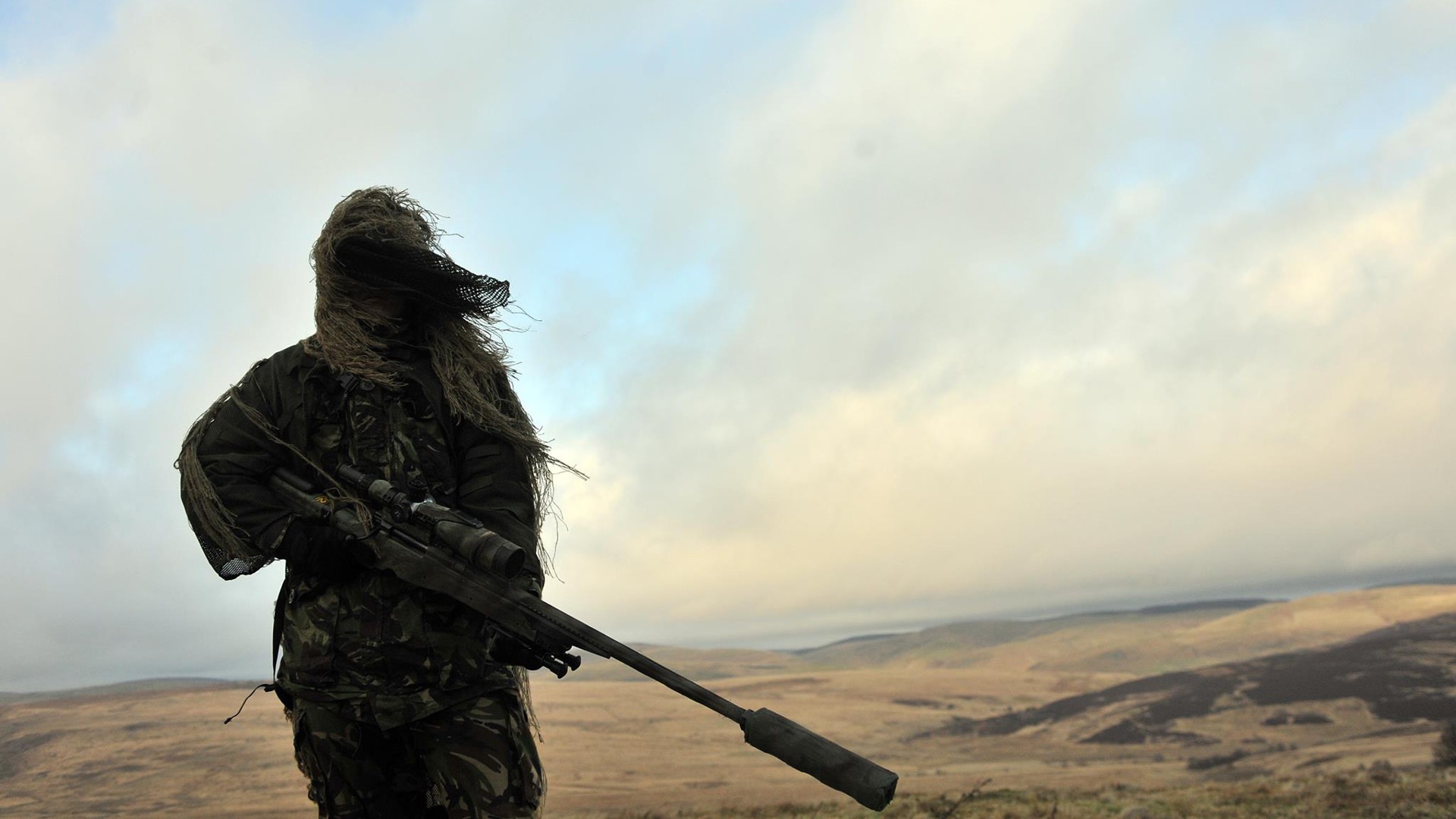 Free photo A desert sniper with a silencer on his rifle.