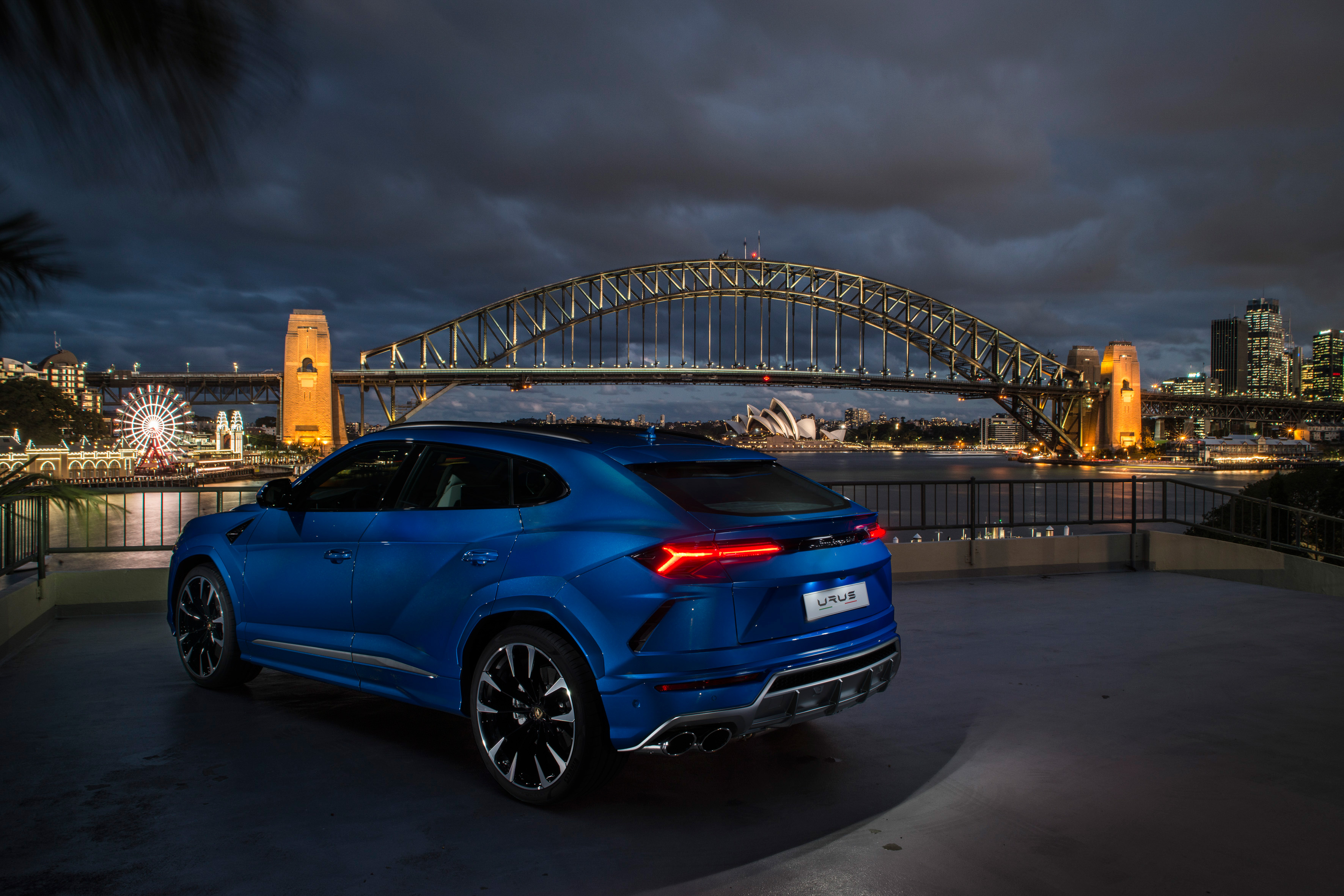 Free photo Blue Lamborghini Urus against the backdrop of a large bridge