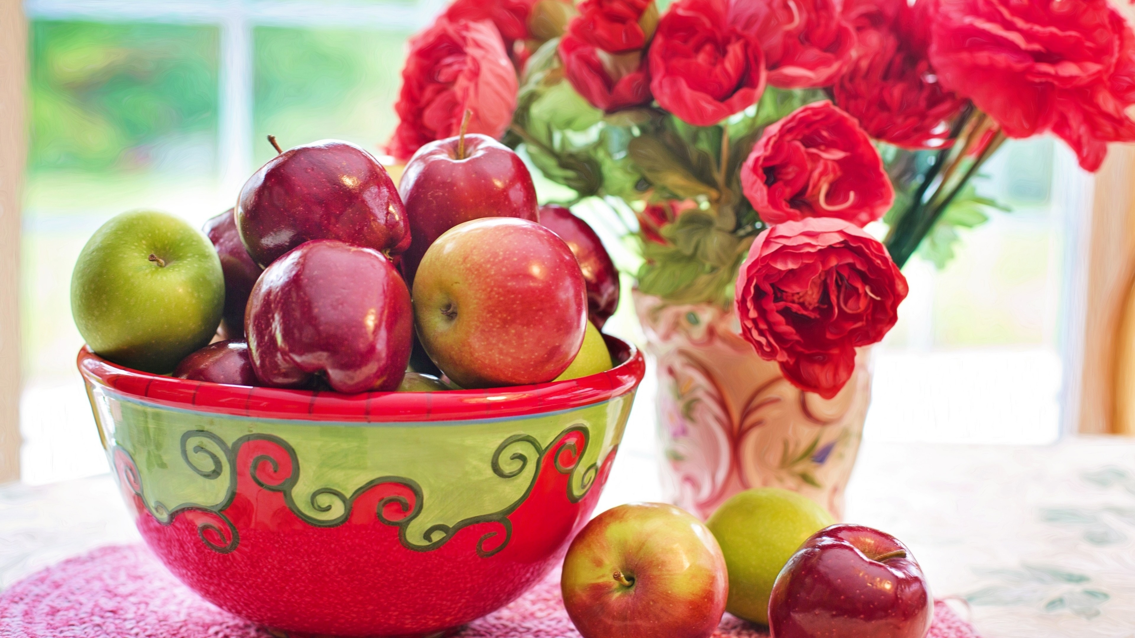 Бесплатное фото Чаша со сладкими яблоками рядом с букетом цветов красного цвета