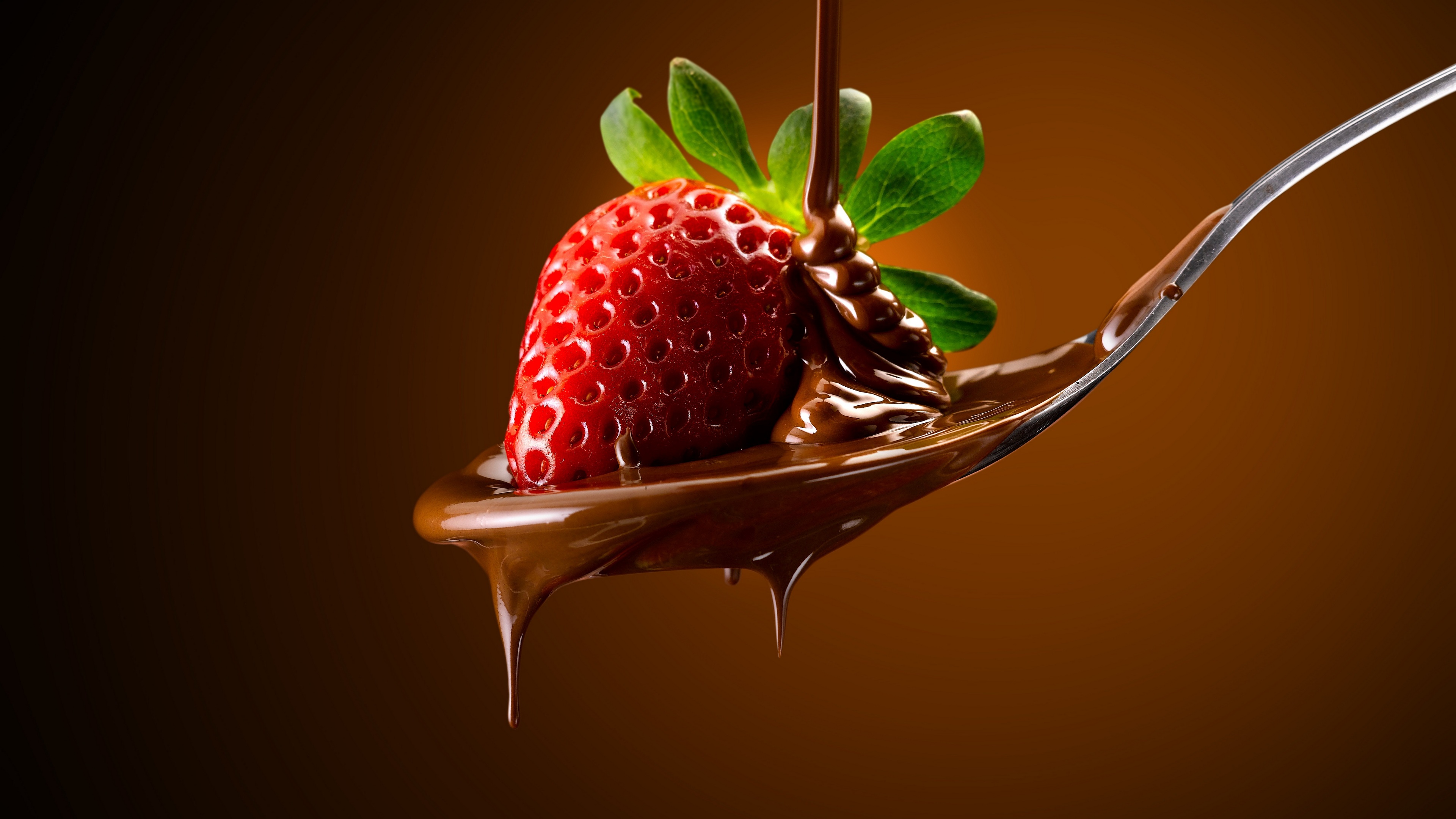 用勺子舀上裹有液态巧克力的草莓