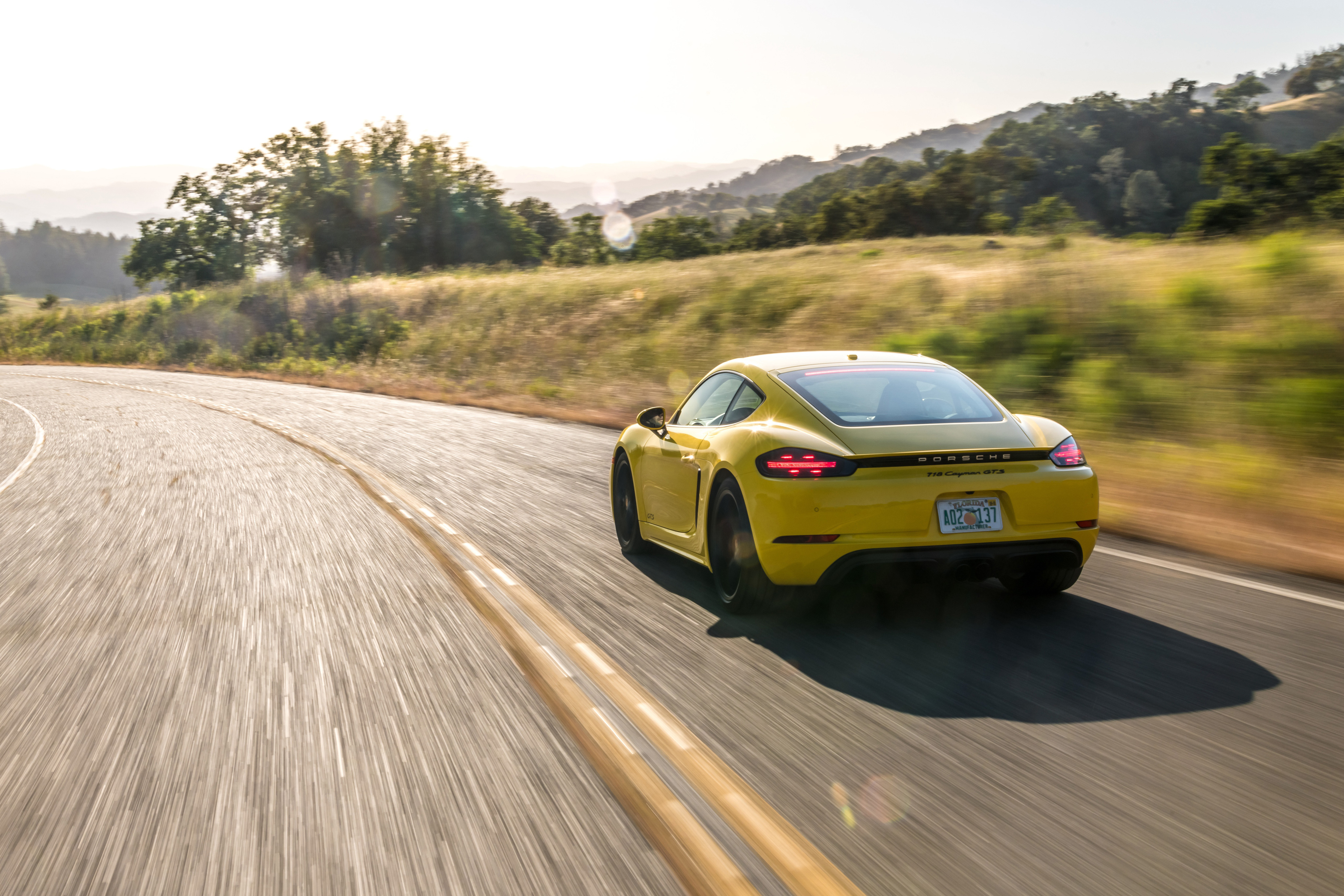 Yellow Porsche 718 driving on a paved road