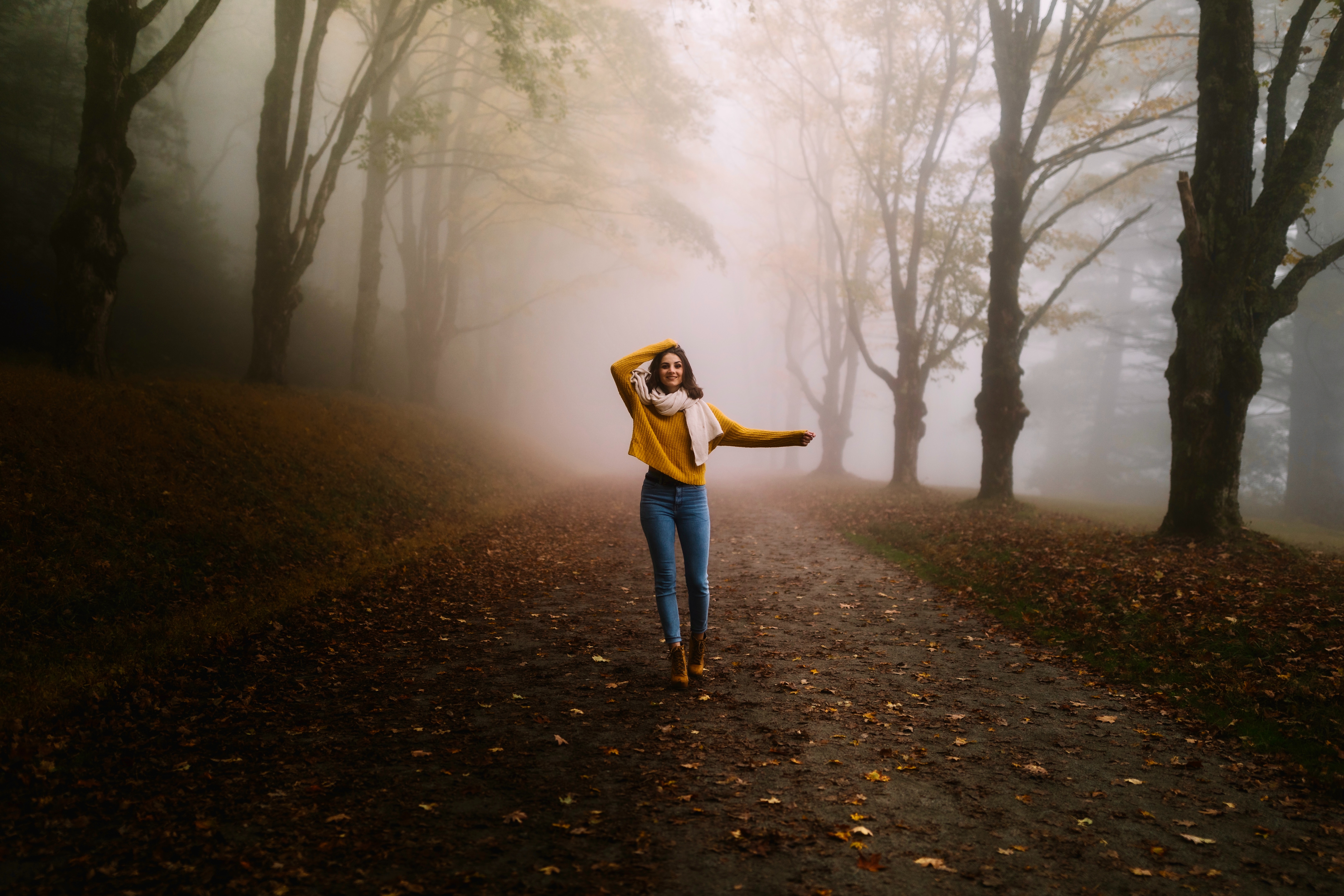 穿着黄色毛衣和牛仔裤的女孩在雾中的秋天的森林里