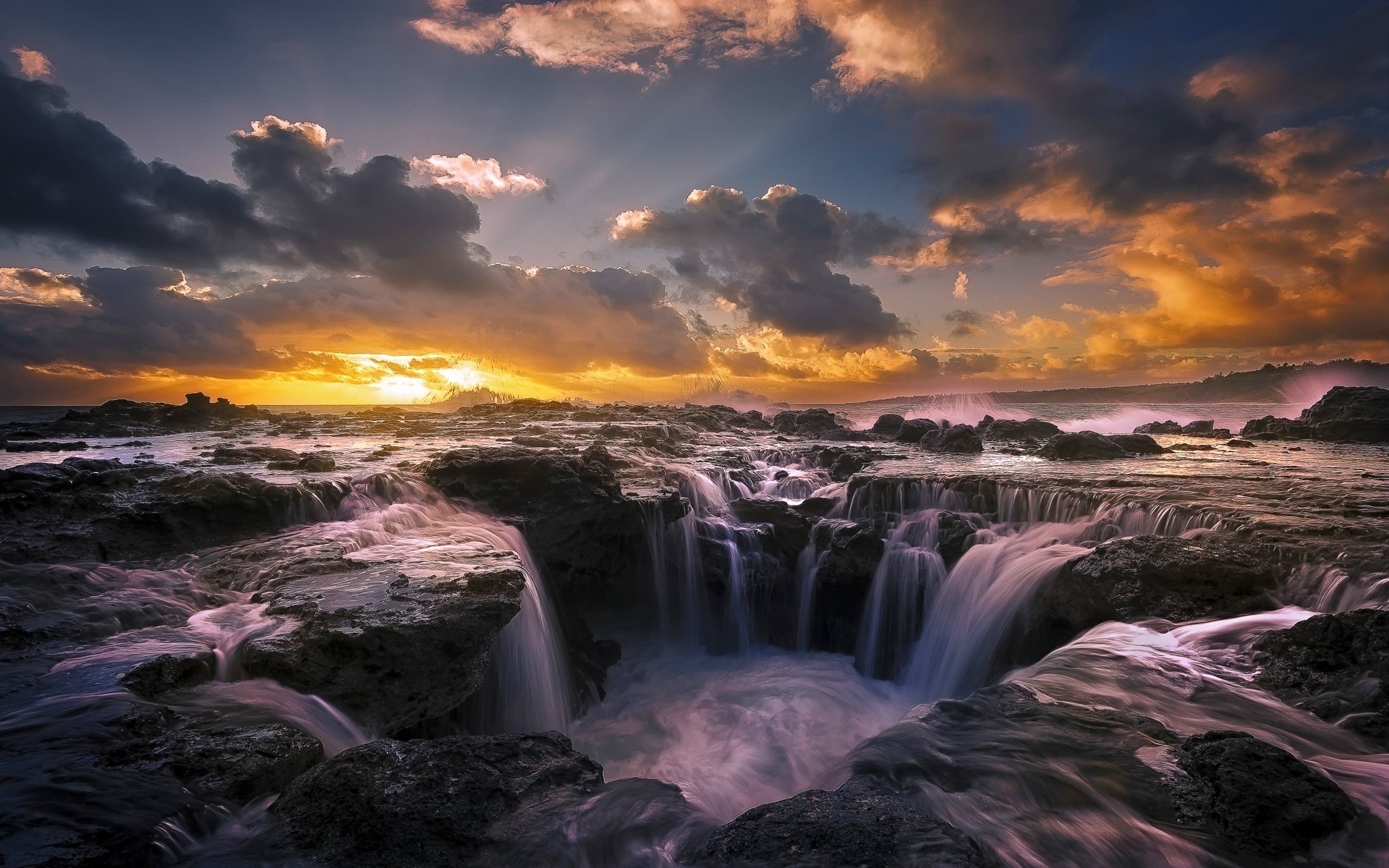 Free photo A landscape with waterfalls washing over a rocky shore and a sunset sky with clouds.