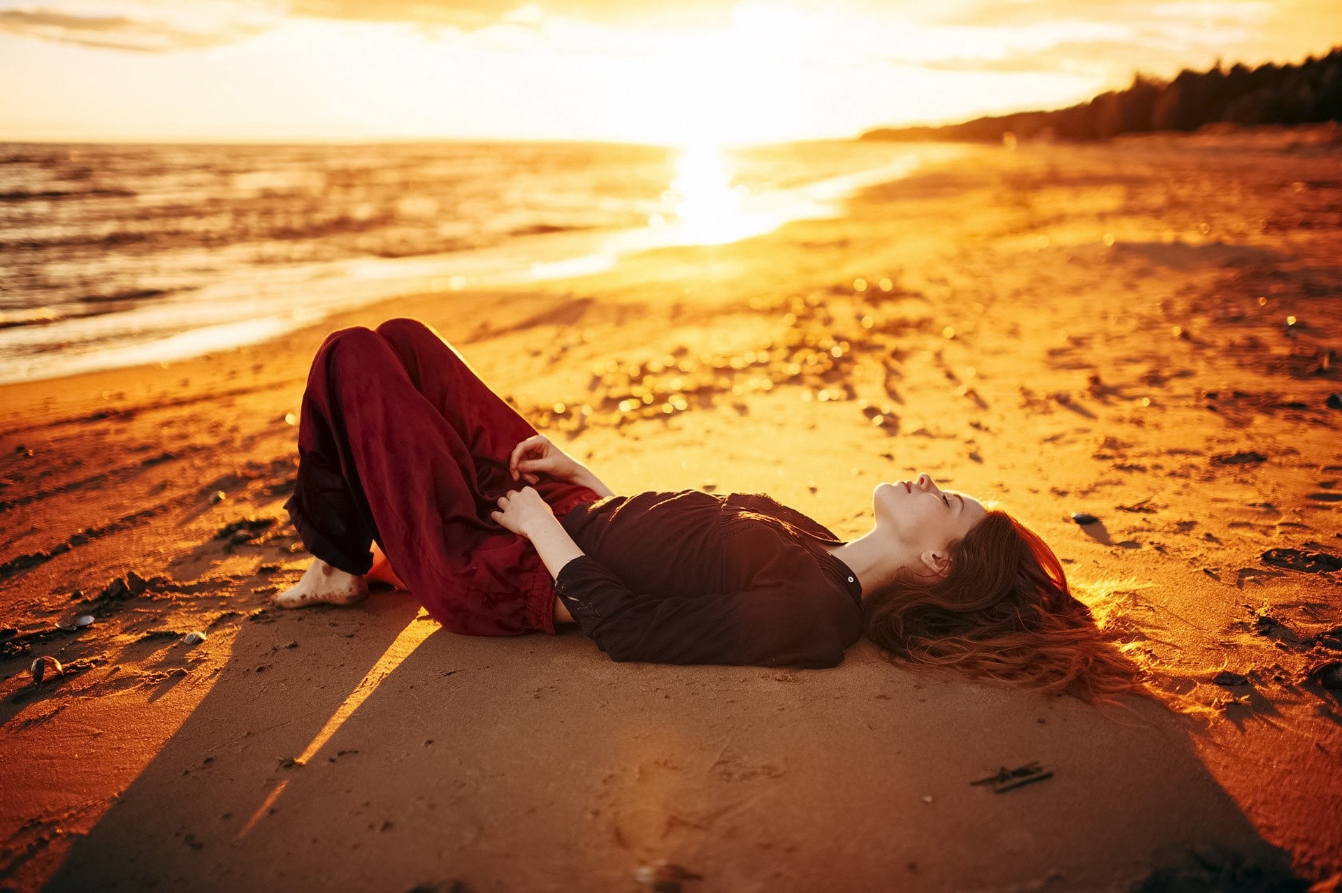 穿着晚装的女孩躺在沙滩上，享受着阳光灿烂的夕阳