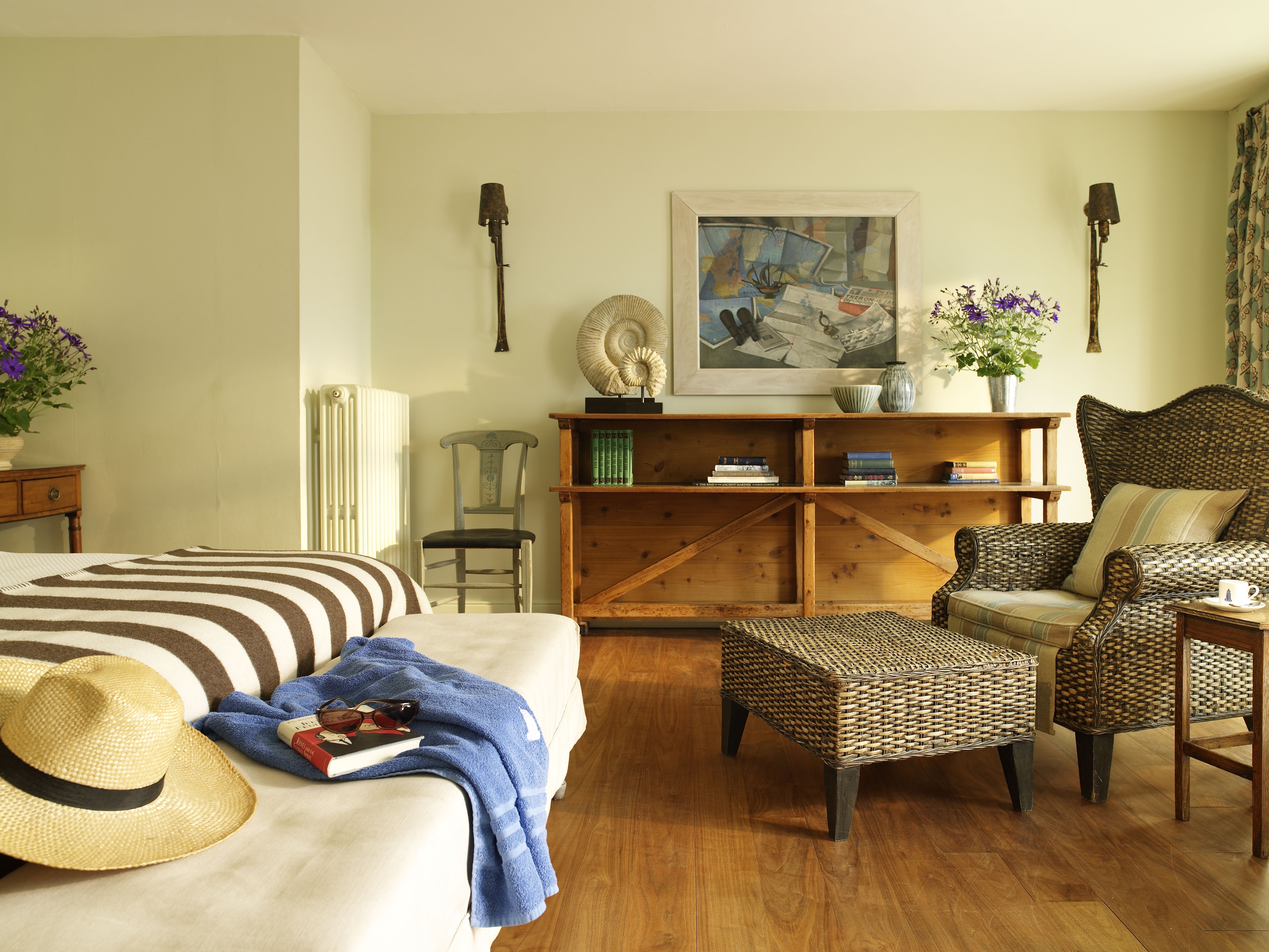 Бесплатное фото Уютная спальня в стиле кантри с деревянной мебелью, плетеным креслом и кроватью с соломенной шляпой и пледом.