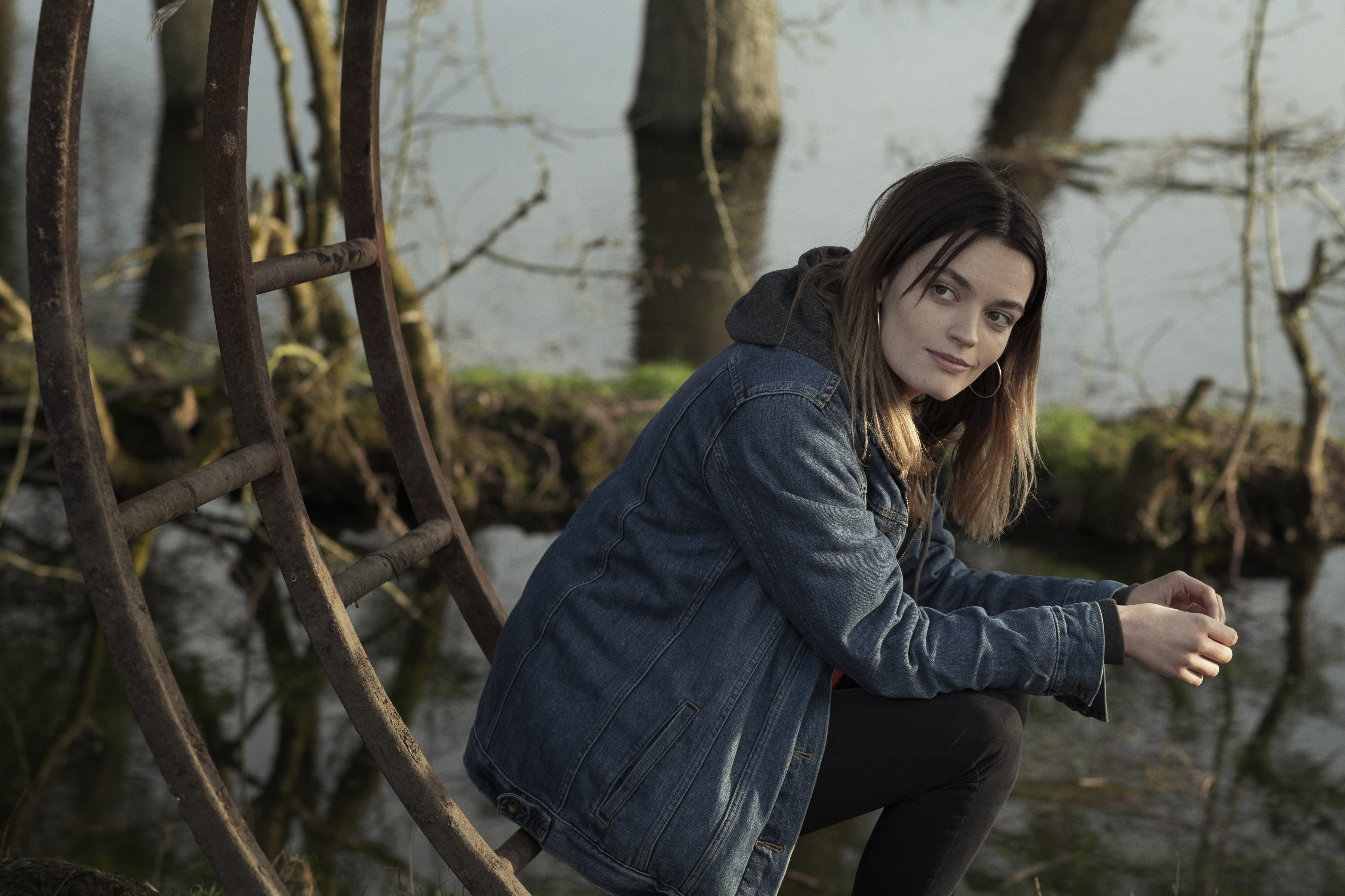 Free photo Emma McKay sits on an iron structure wearing a denim jacket