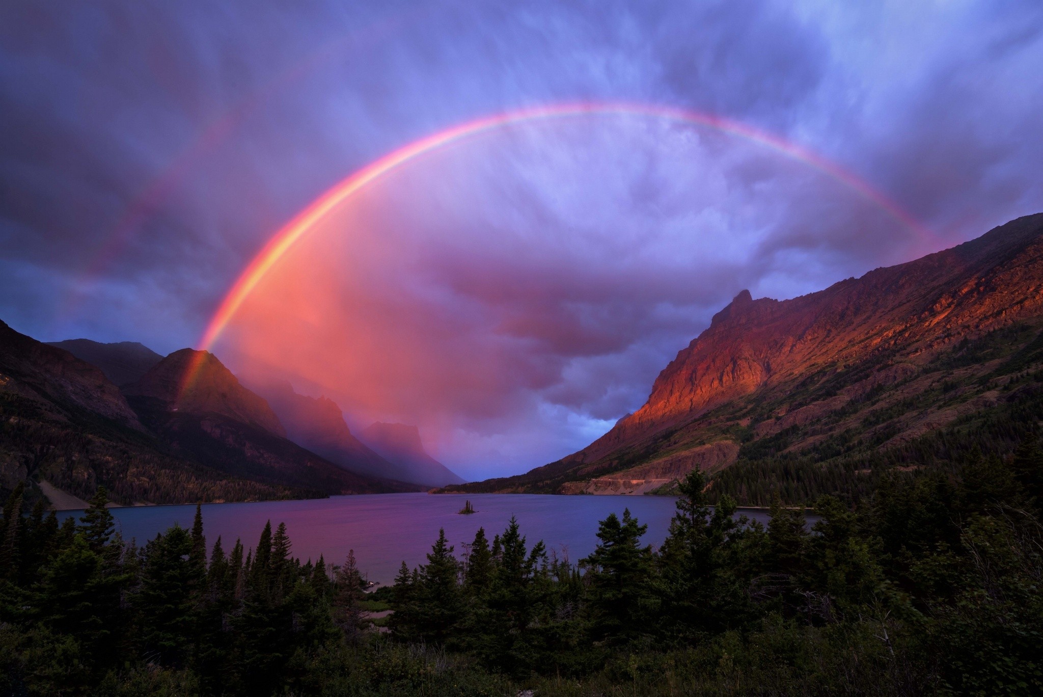 A lake in the mountains with a rainbow spanning the entire scene, creating a fantastic and majestic landscape.