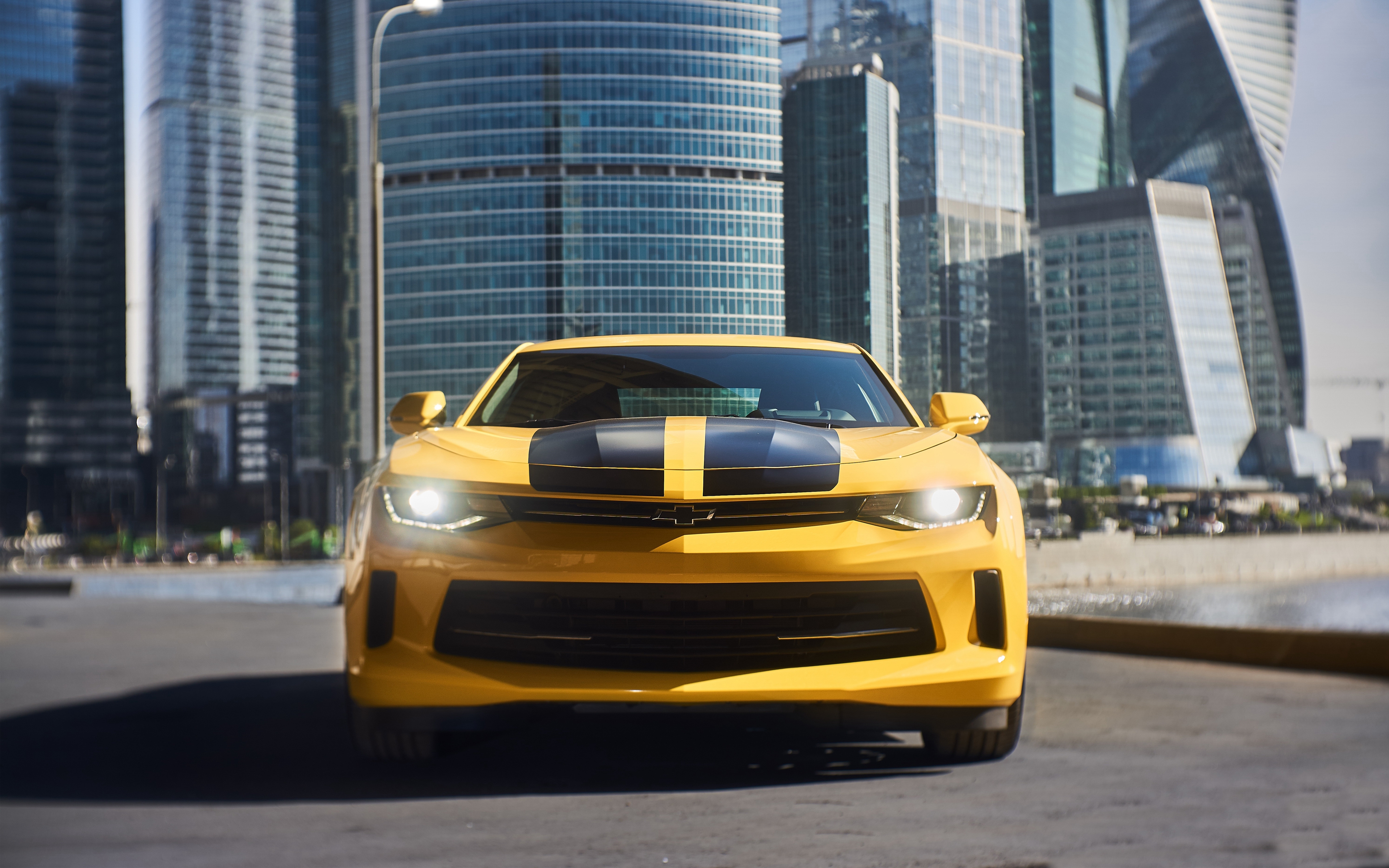 Бесплатное фото Желтый Chevrolet Camaro с черными полосами на капоте на фоне небоскреба Москва Сити