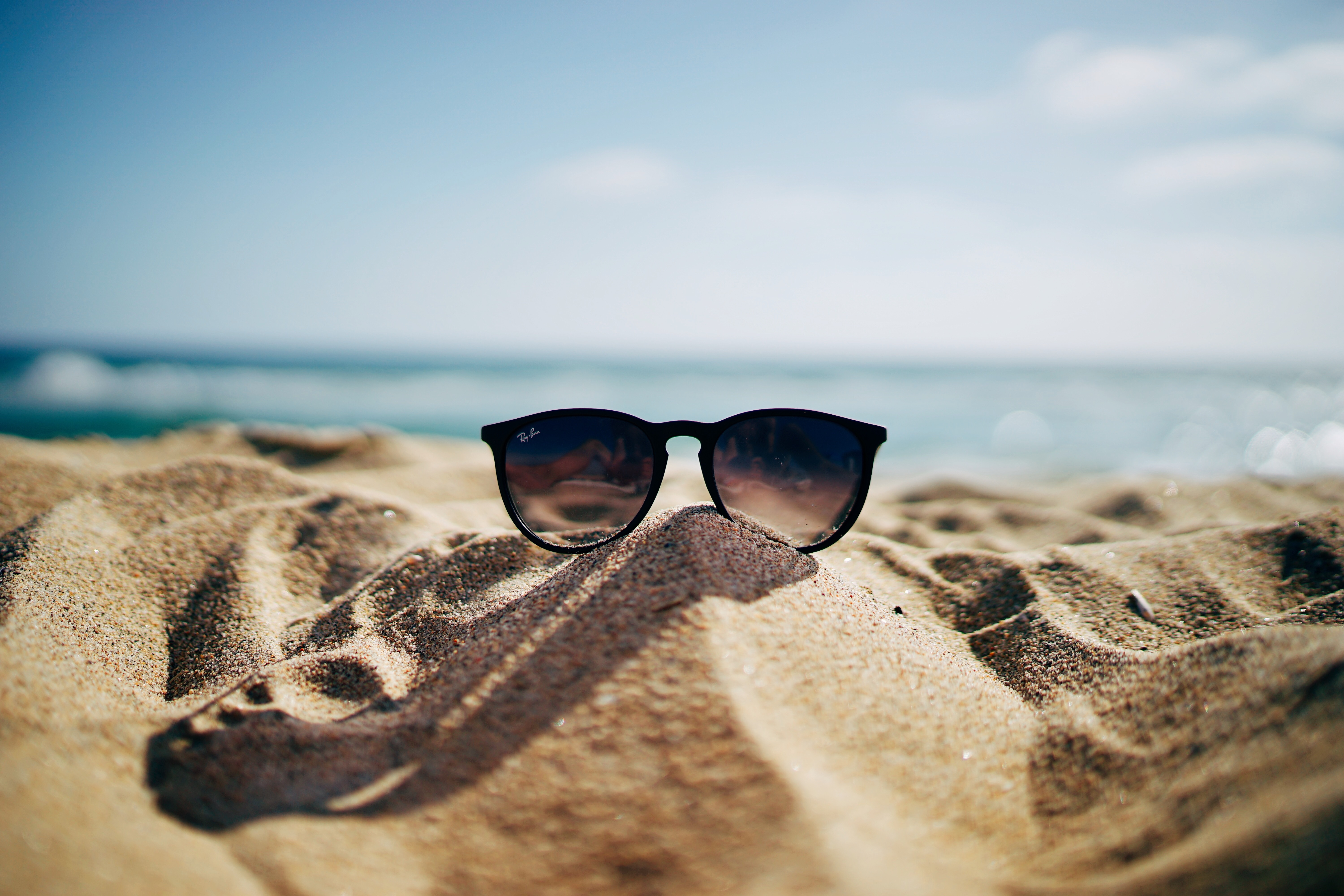 Free photo Ray Ban sunglasses on a sandy beach.