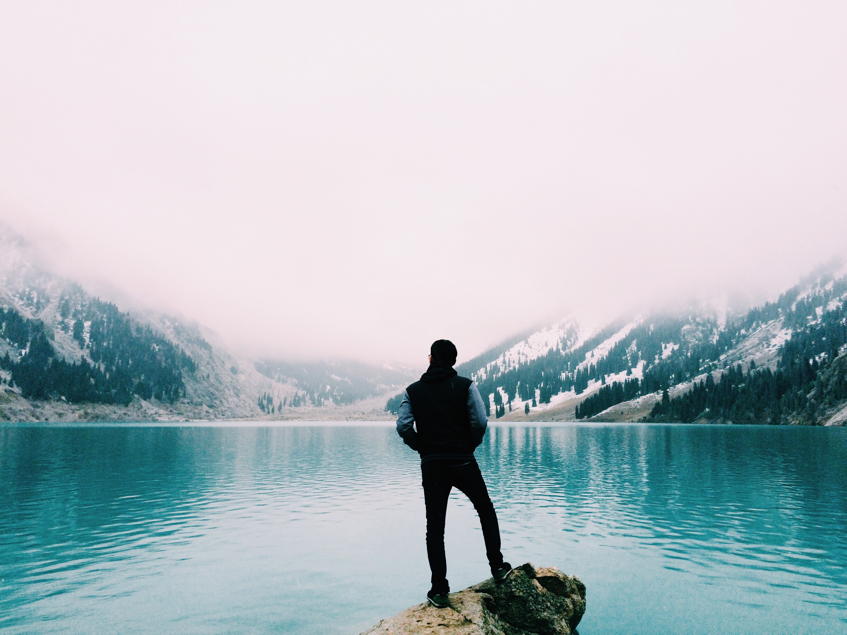 Free photo A guy admires the fog over the lake standing on a big rock.