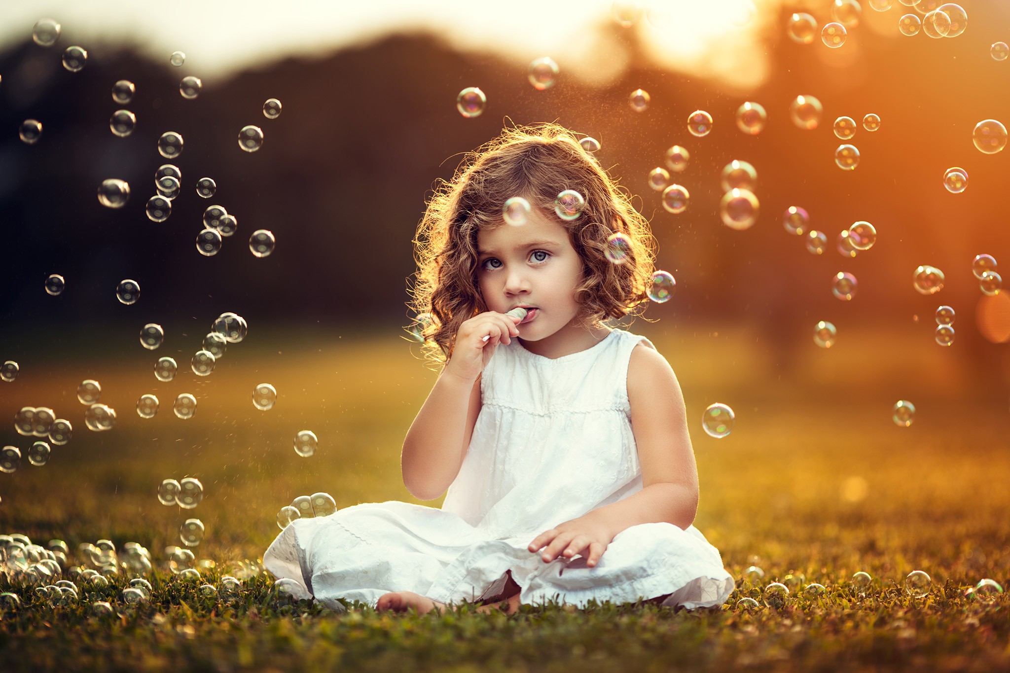 A little girl in a white dress blowing soap bubbles