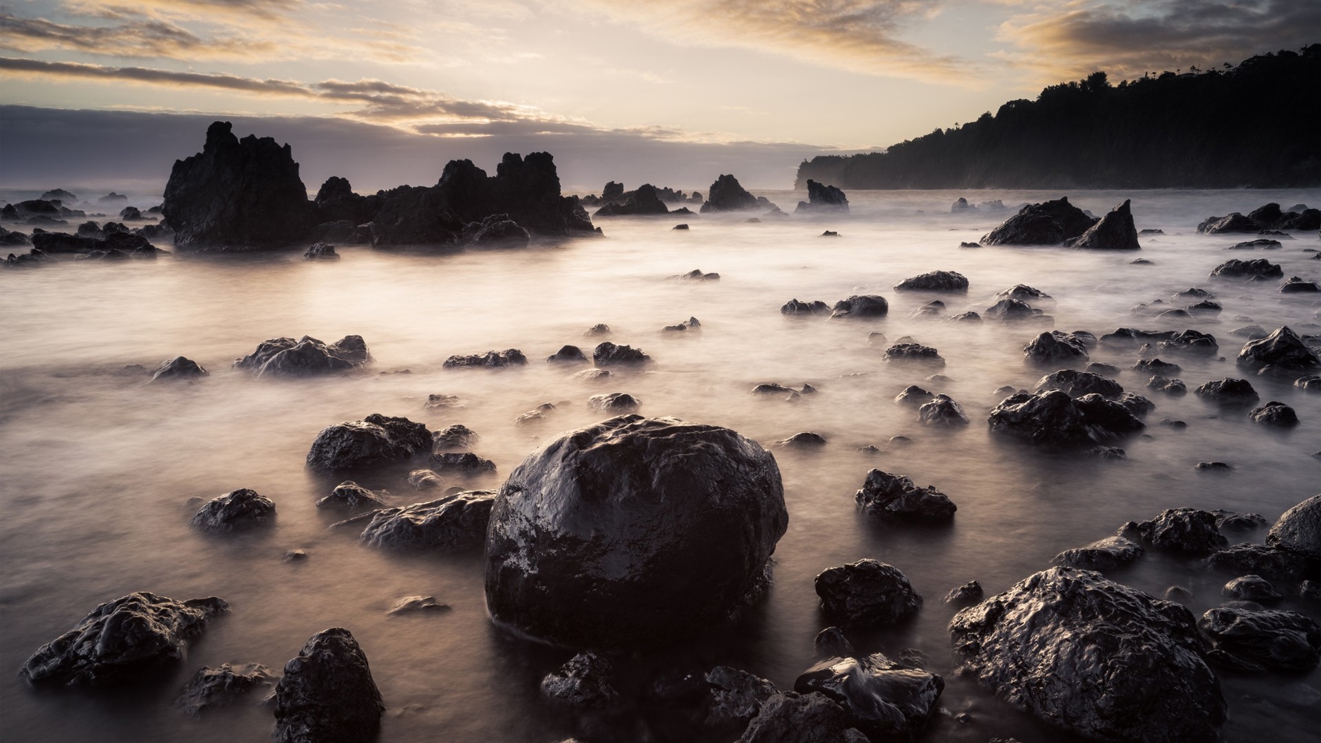 Free photo A tranquil seascape with stones on the shore reflecting the light and rocky cliffs in the background.
