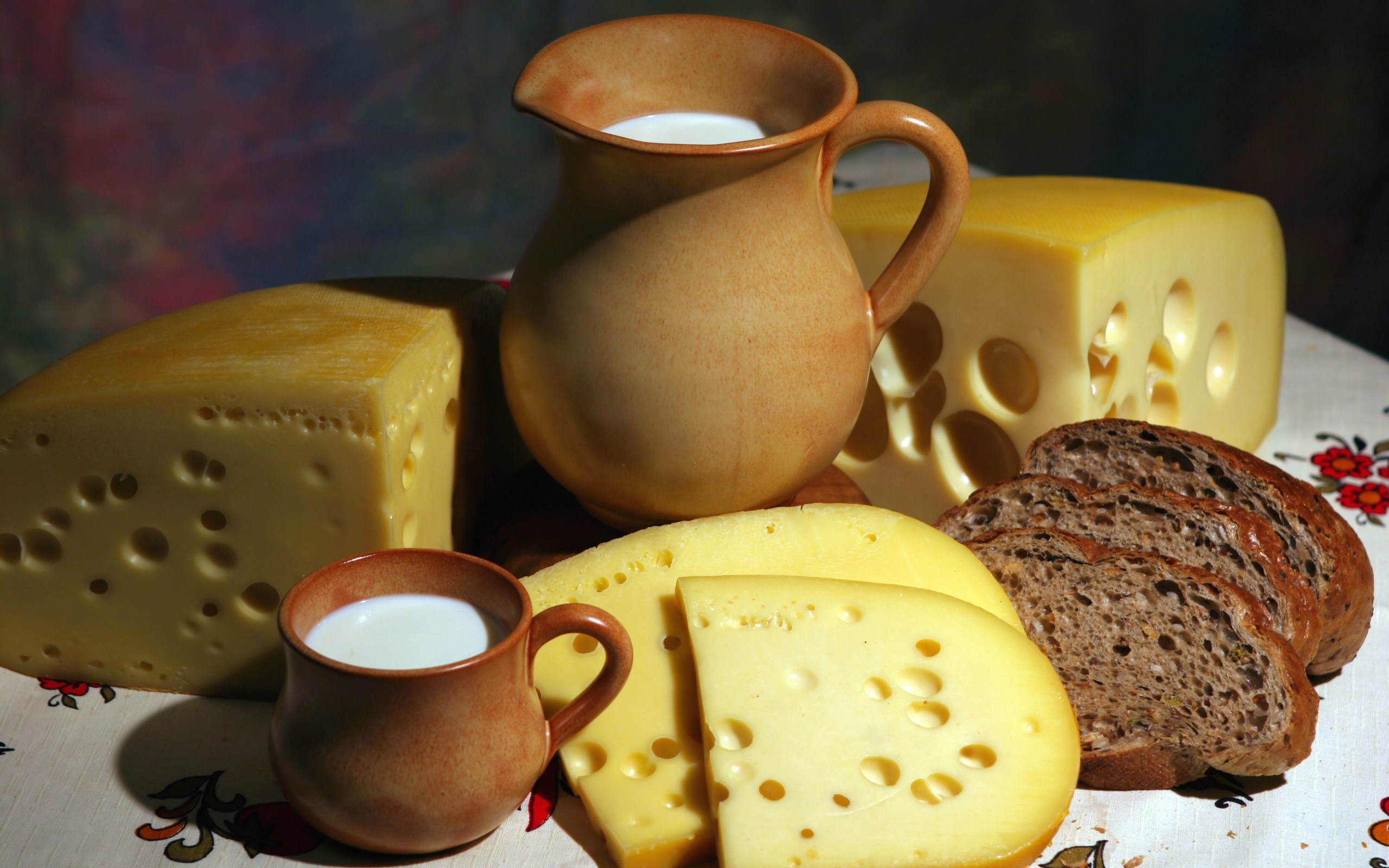 Free photo Pieces of leaky cheese, an earthenware jug and a cup of milk sit side by side with slices of rye bread on the table.