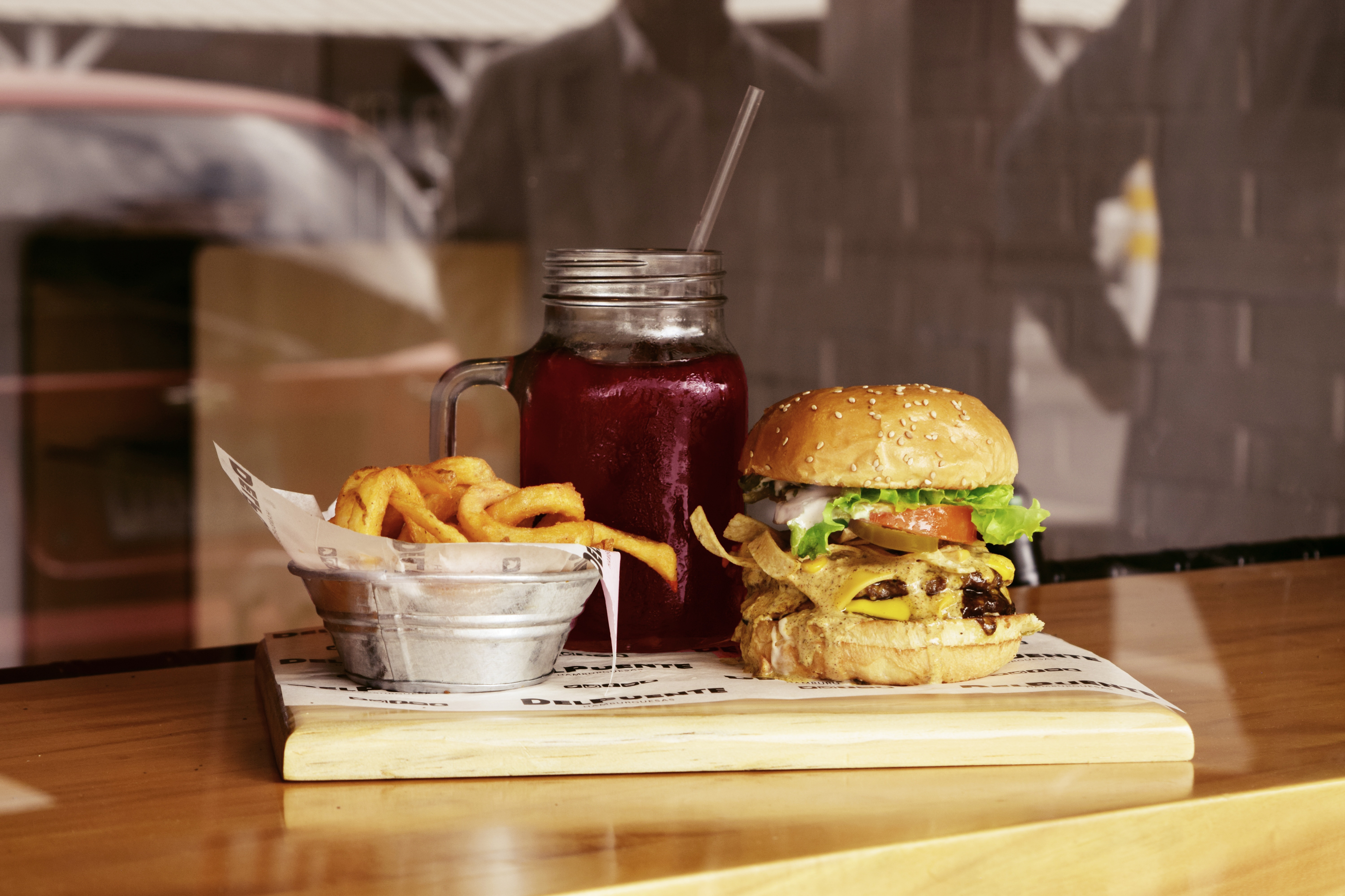 A juicy burger with cheese and herbs, a portion of fries and a berry drink in a jar - an appetizing set on a wooden tray.