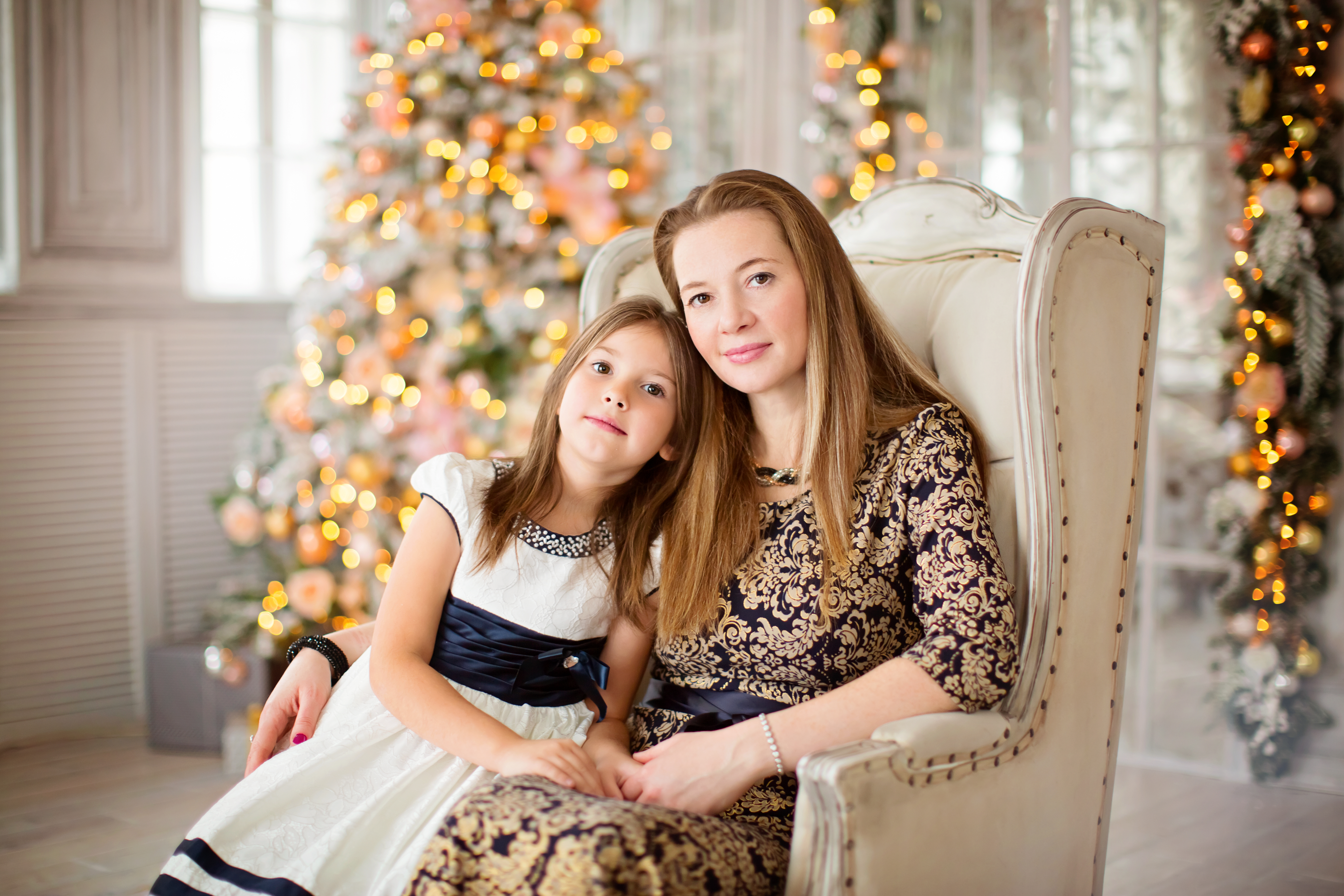 免费照片一位美丽的女士和她的女儿坐在圣诞树旁的椅子上。