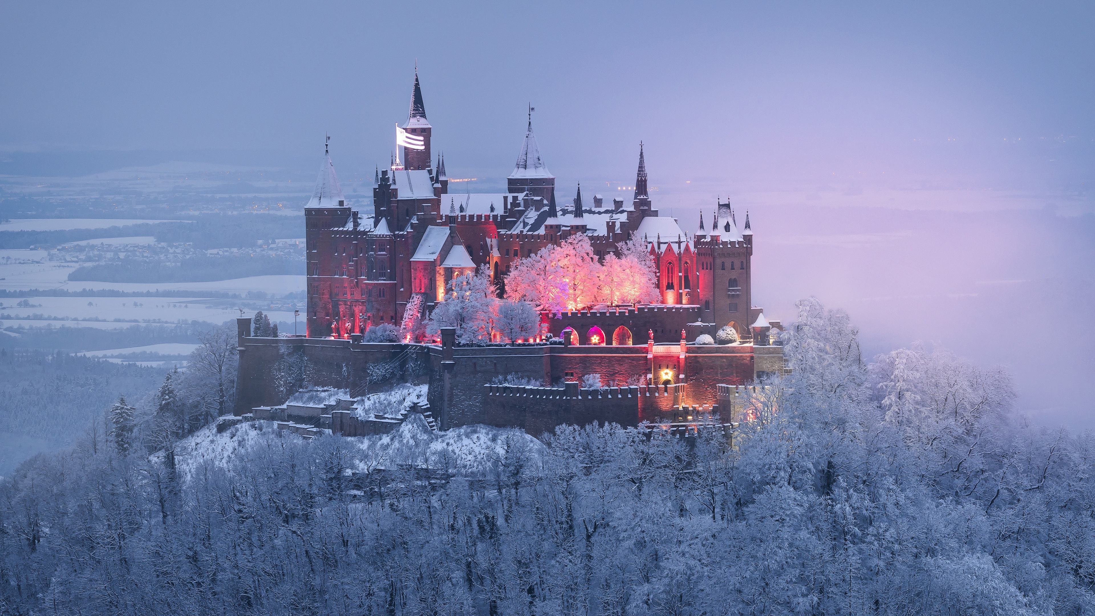 A large castle in Germany on top of a mountain in a winter forest