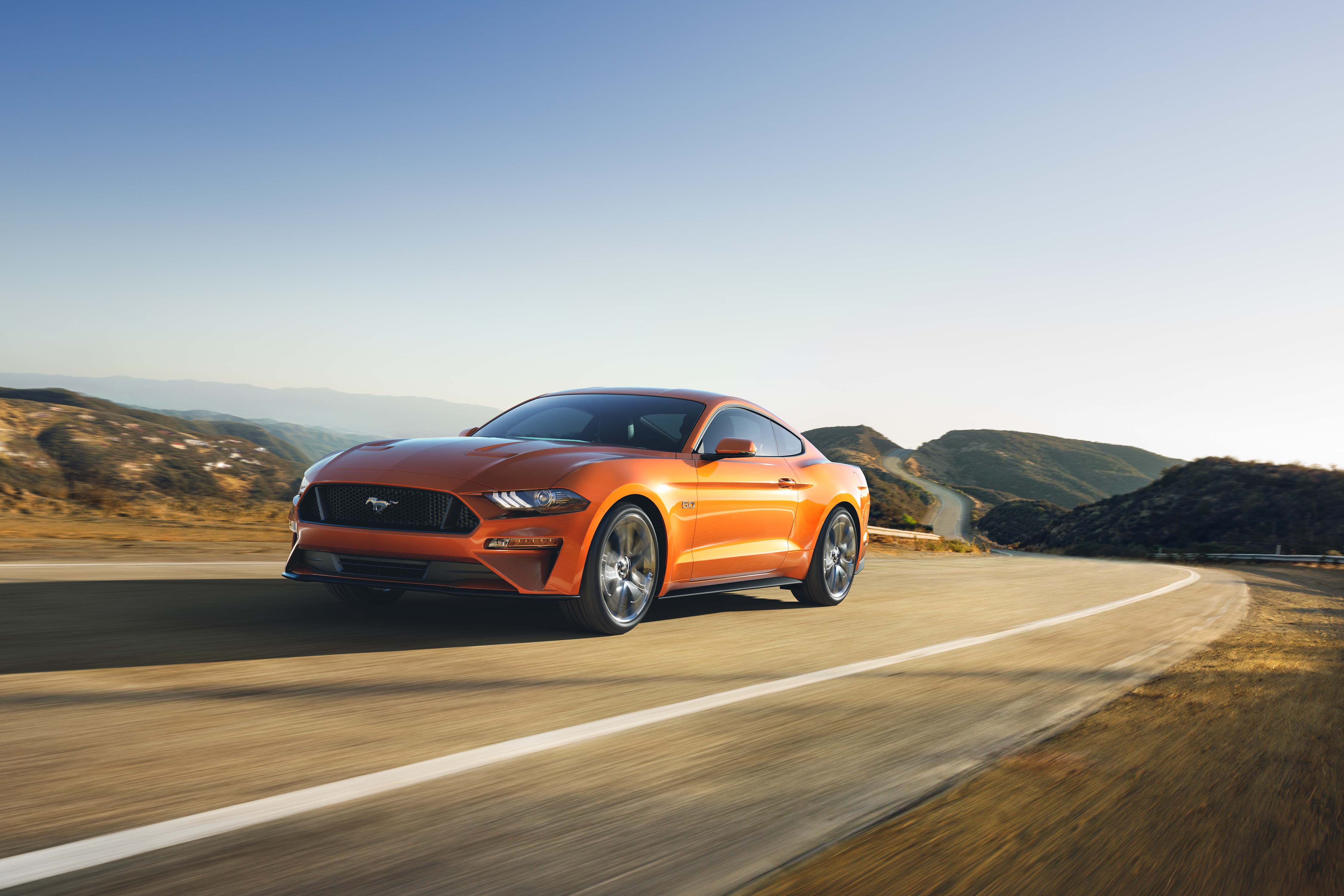 Free photo An orange Ford Mustang drives down a country road