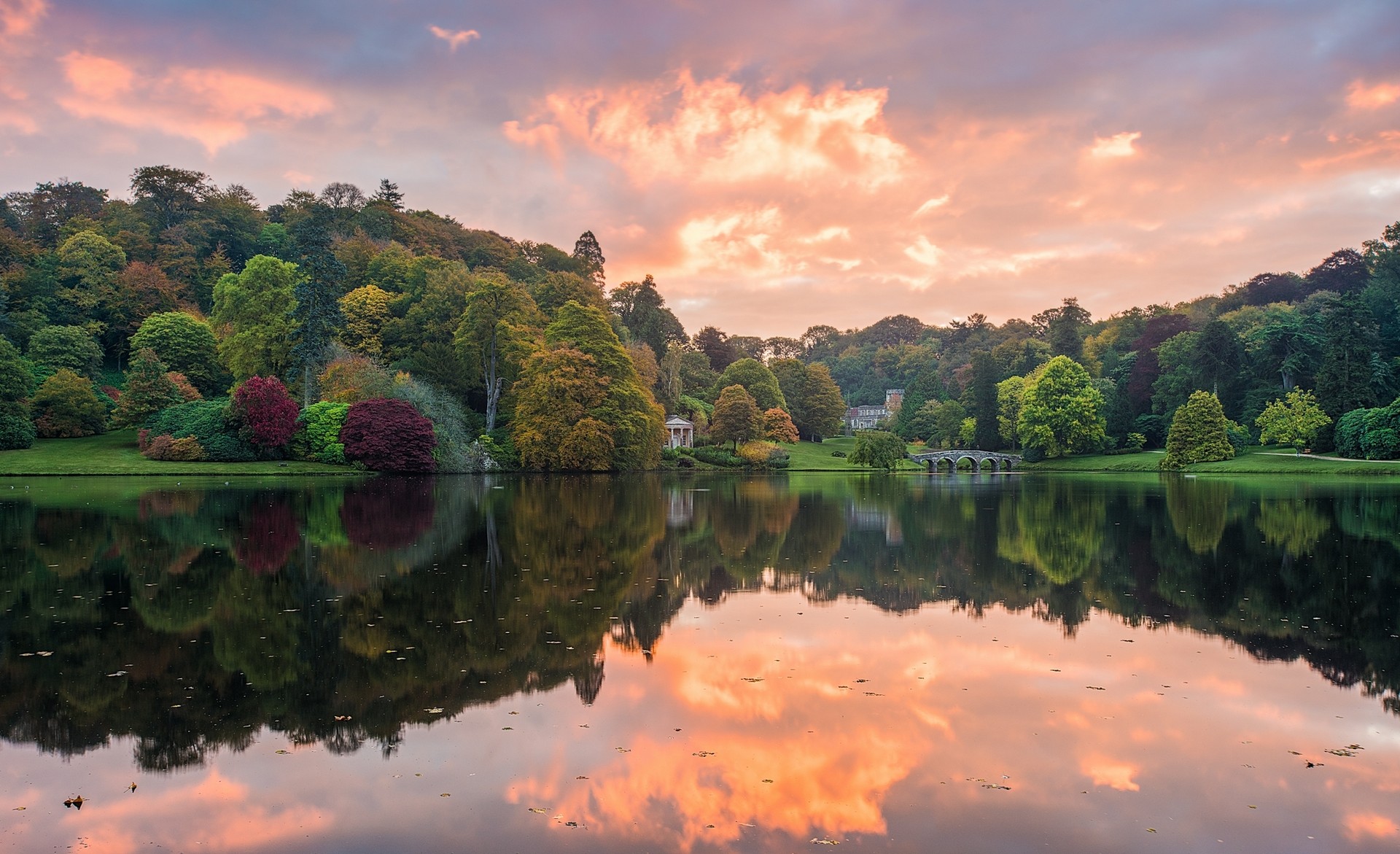 Бесплатное фото Живописный пейзаж с озером, отражающим закатное небо, окруженным деревьями и зданием на заднем плане.