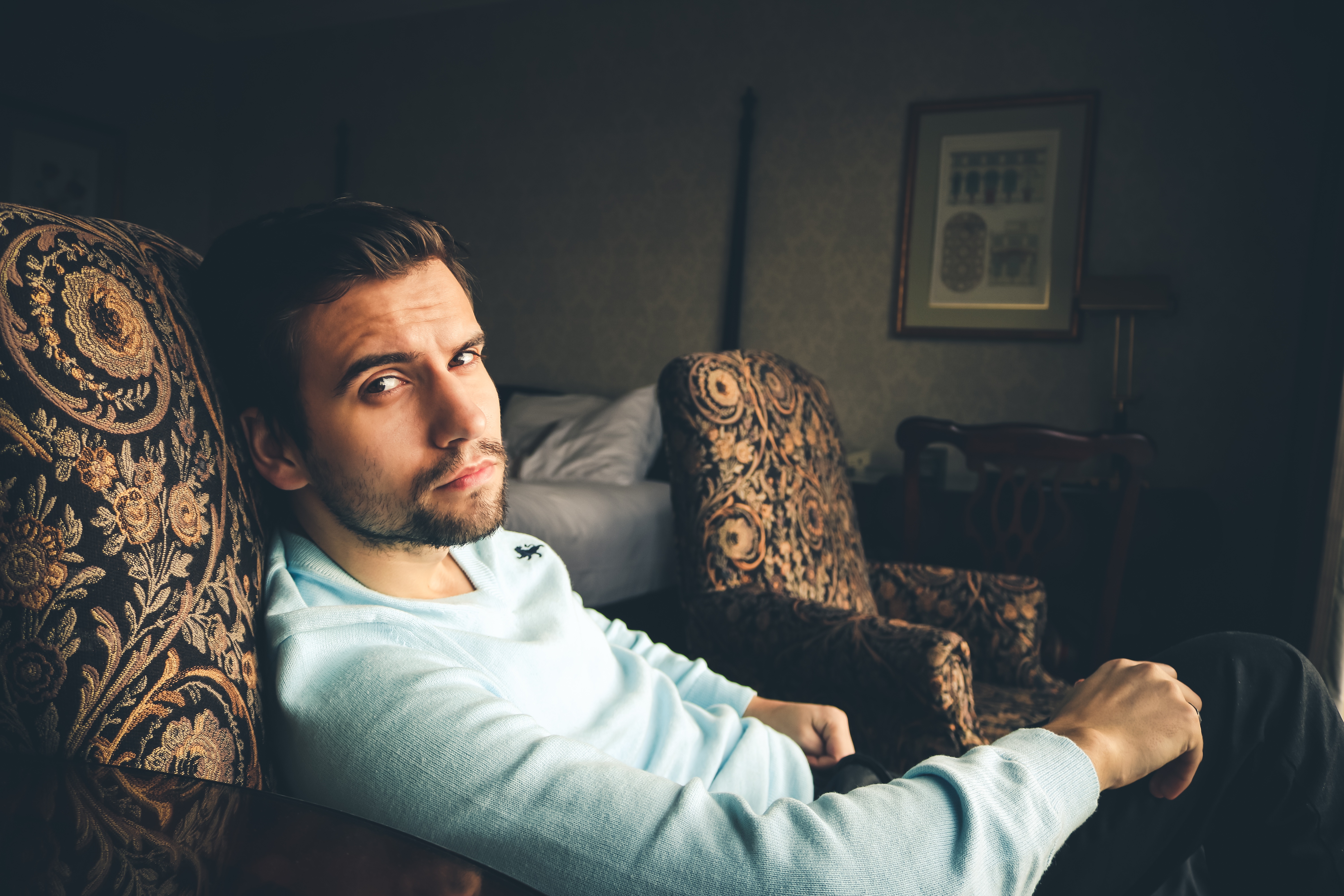 Free photo A young guy in a white turtleneck sits in an armchair