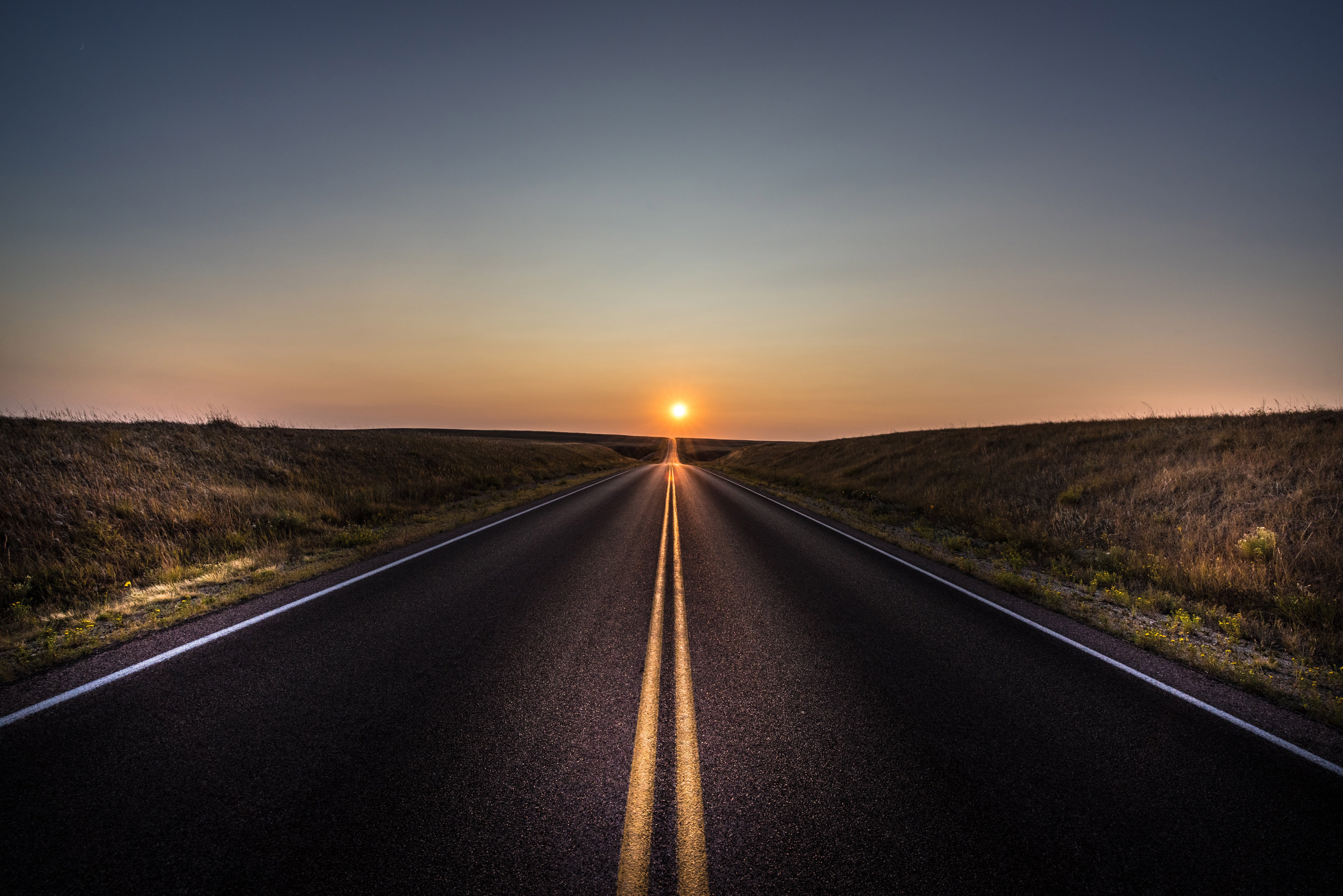 Free photo A long paved road leading to the sun.