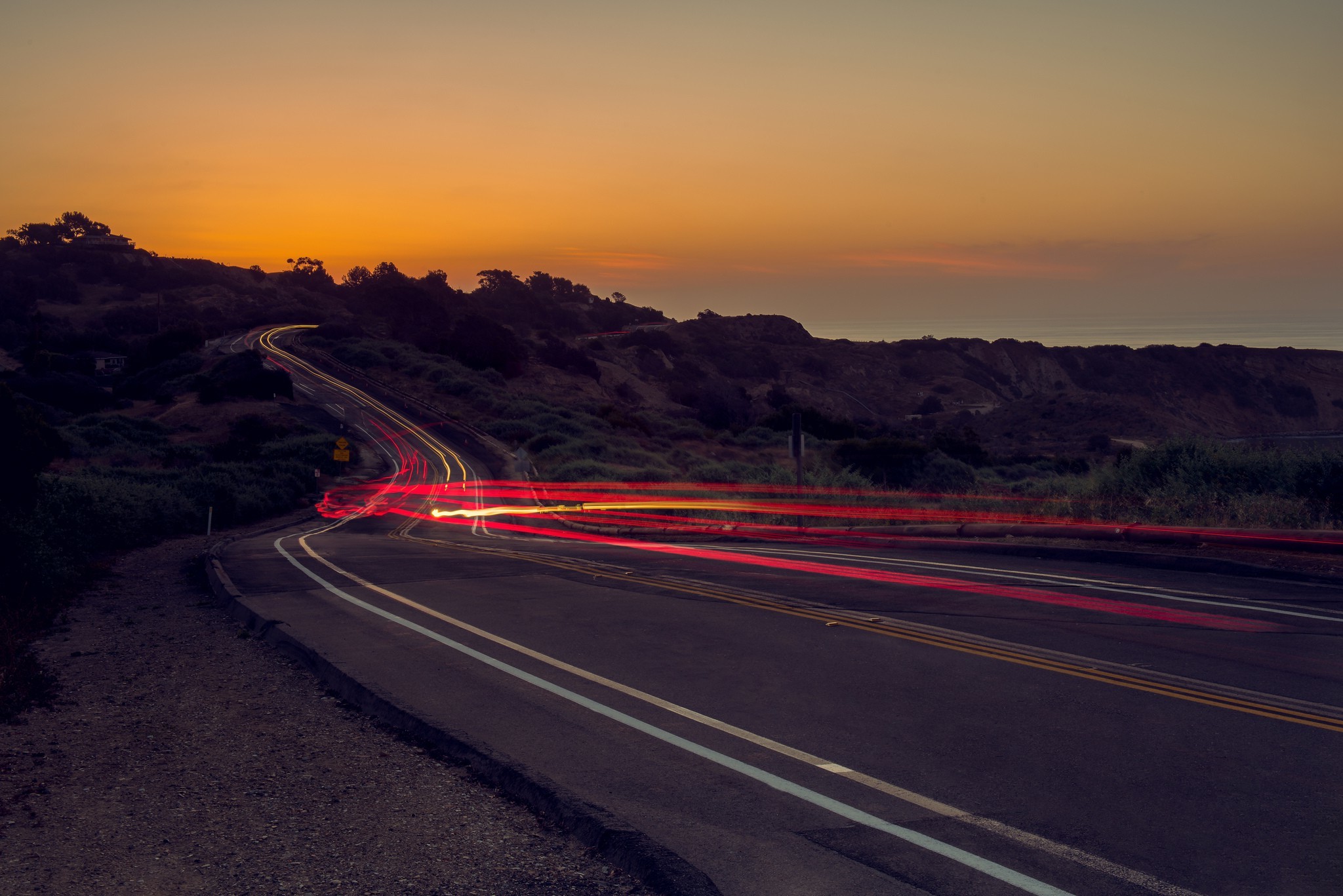 Free photo Sunset on the highway with hills and light trails from cars.