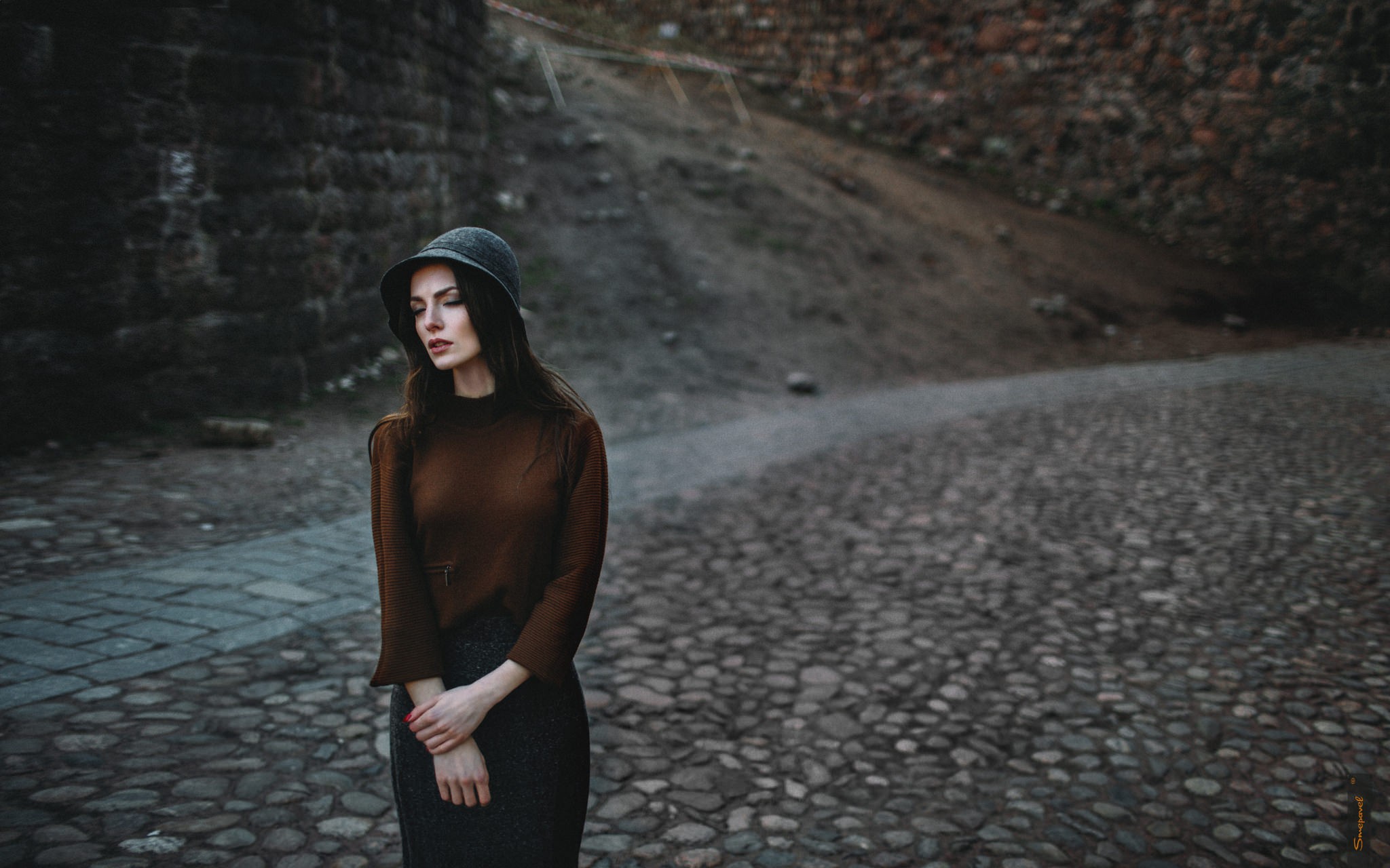 A girl in a hat walks the gloomy streets.