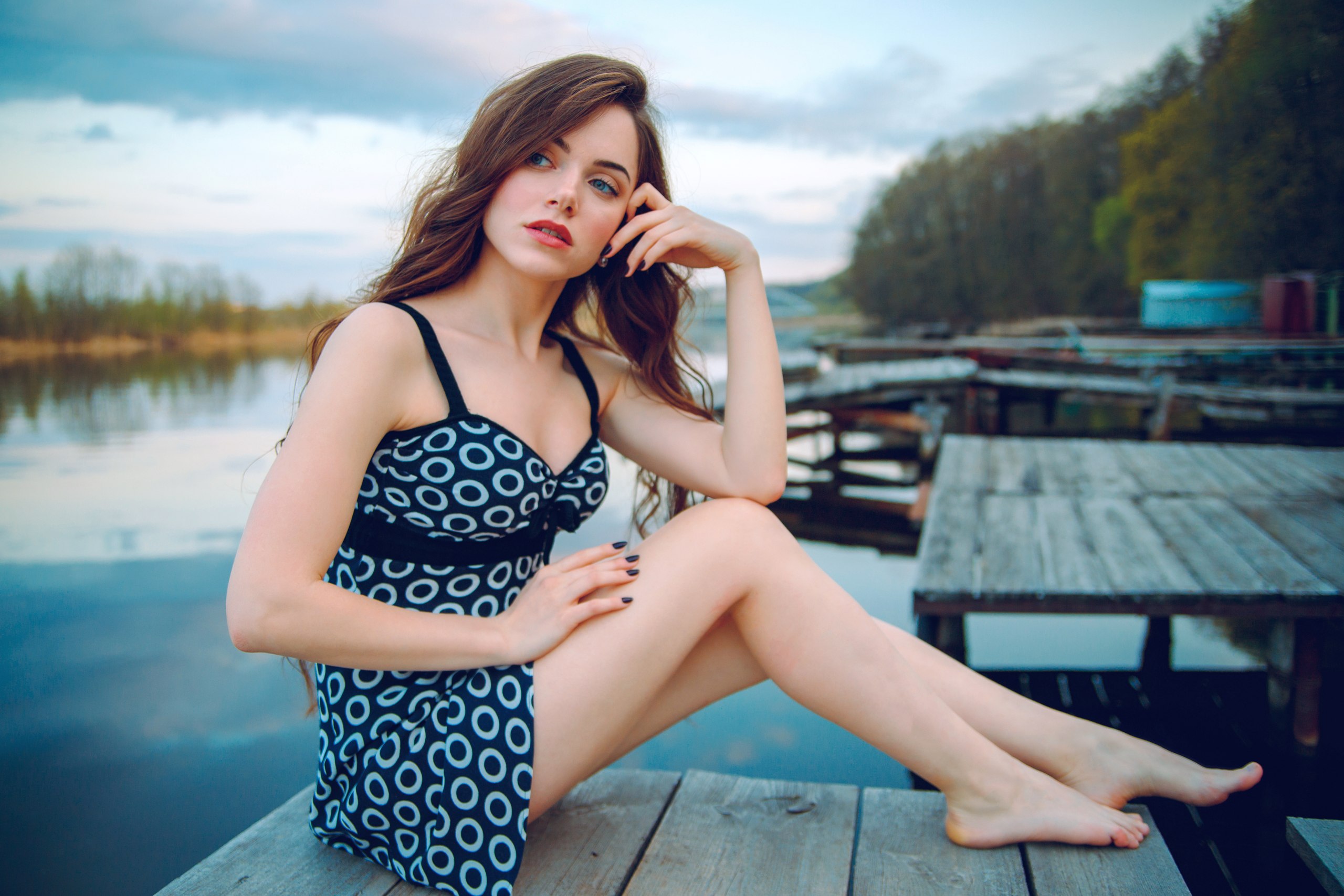 A girl in an evening dress sits on a wooden bridge