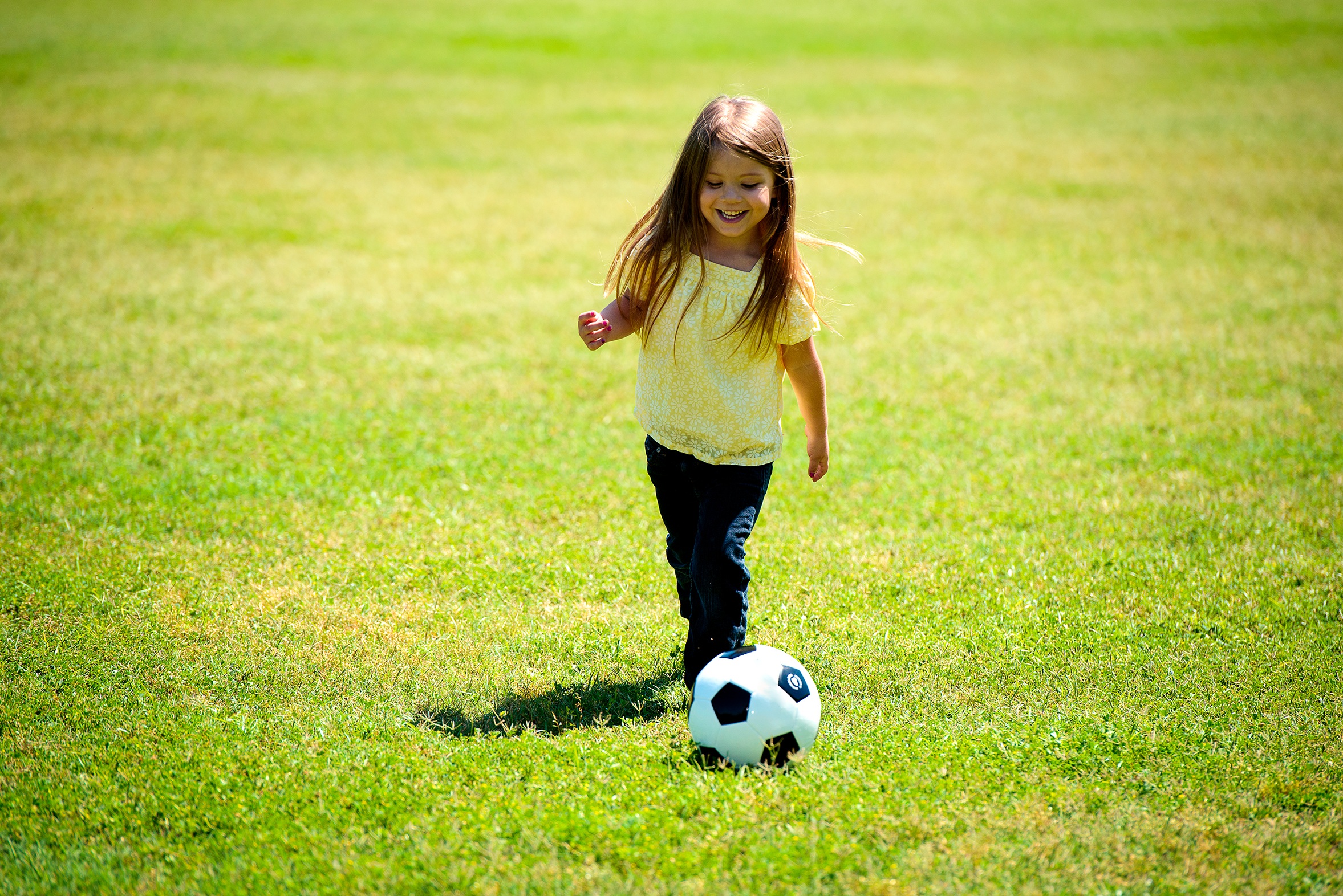 Free photo A little girl plays with a soccer ball on a green lawn