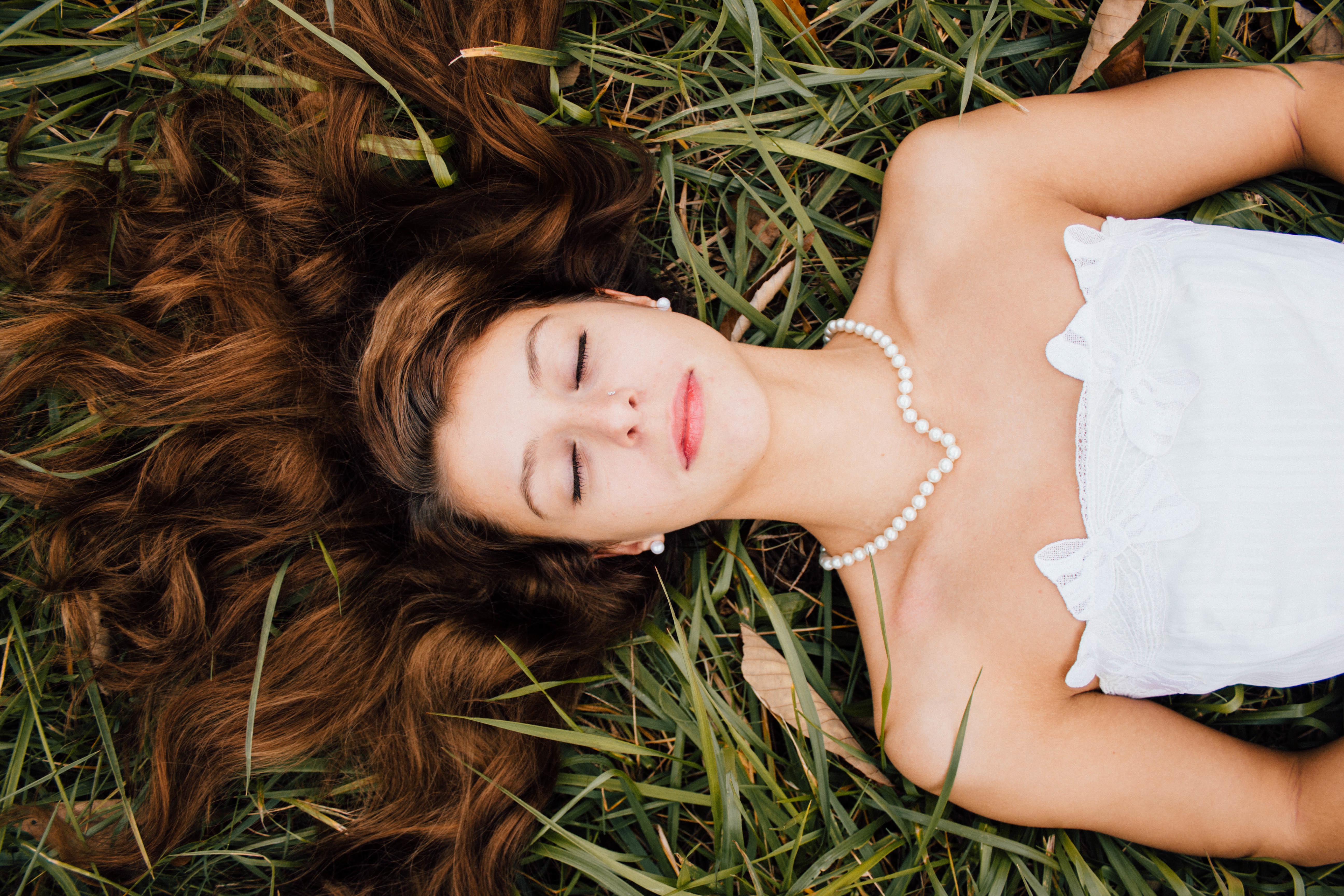 一个身穿白色连衣裙的黑发女子躺在绿色的草地上